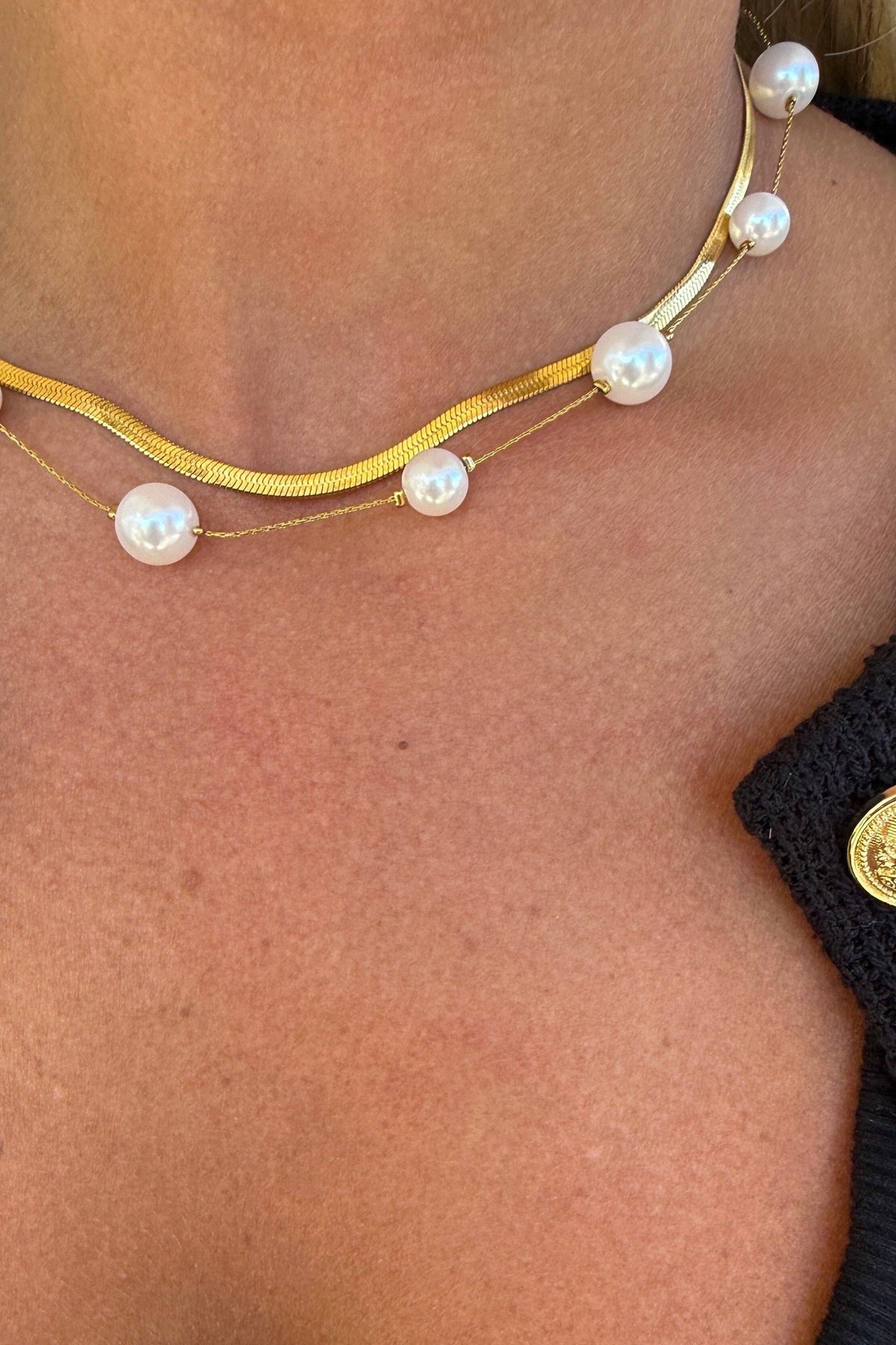 Gold necklace with pearls worn by a person, close-up view.