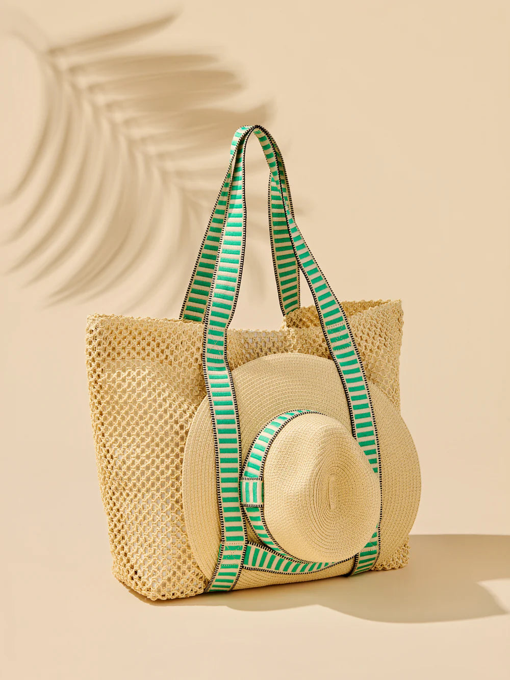 Woven straw bag with green striped handles on a beige background