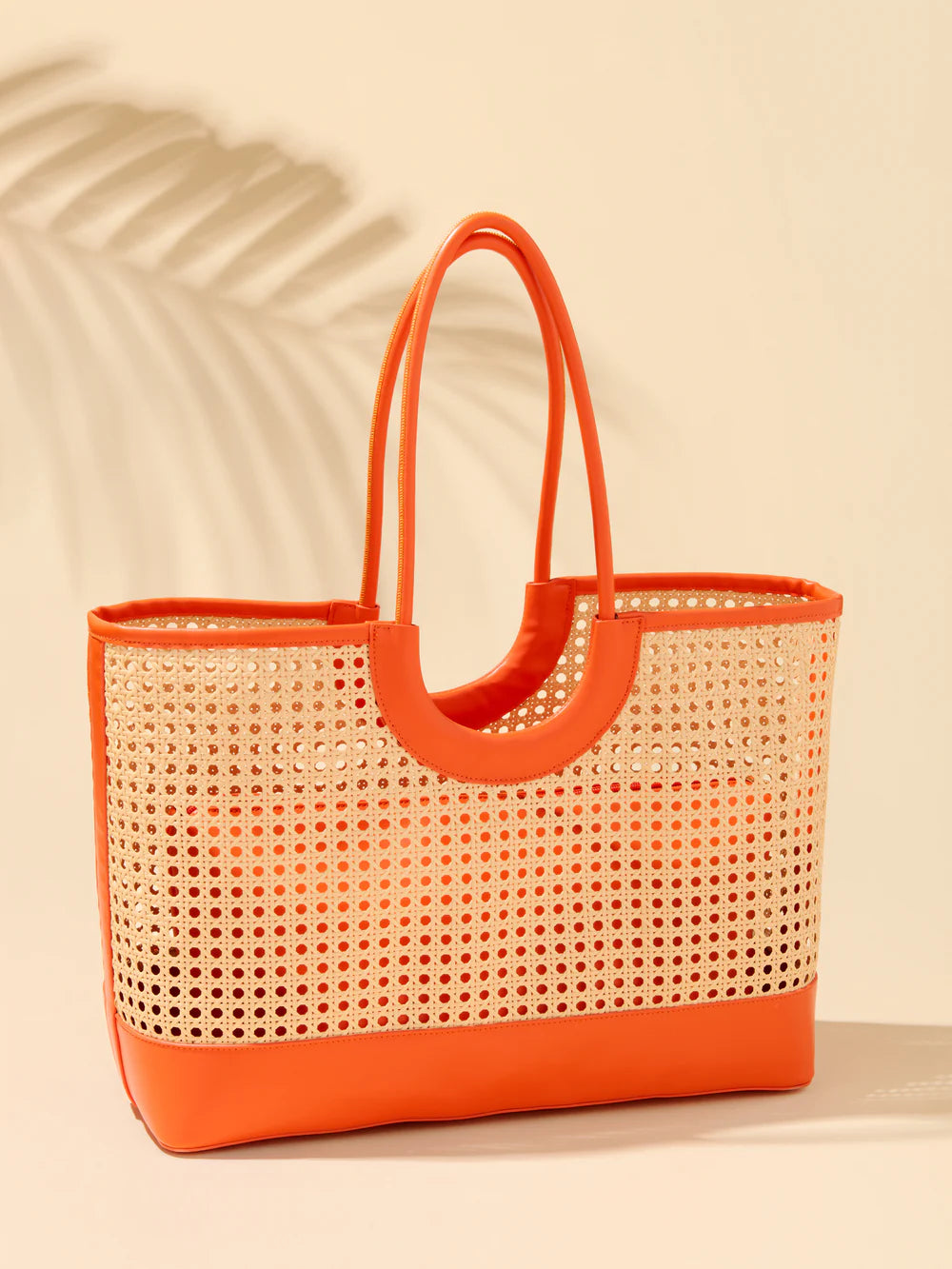 Woven tote bag with orange handle and trim on a beige background