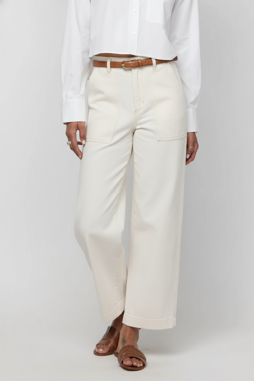 Person wearing a white shirt and cream-colored wide-leg pants with a brown belt on a plain background