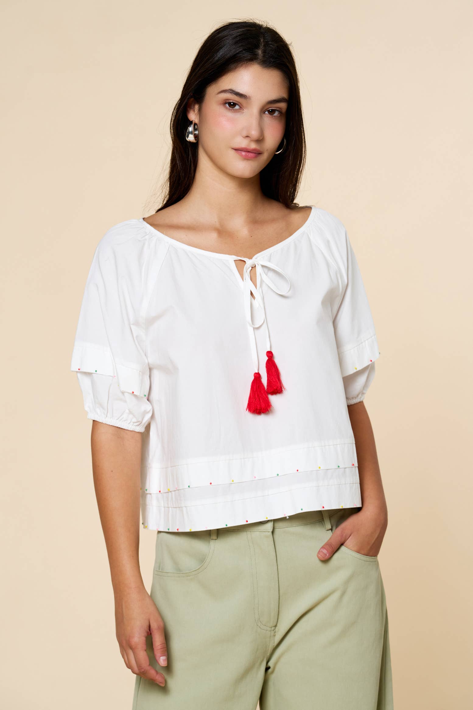 Woman wearing a white blouse with red tassels on a beige background