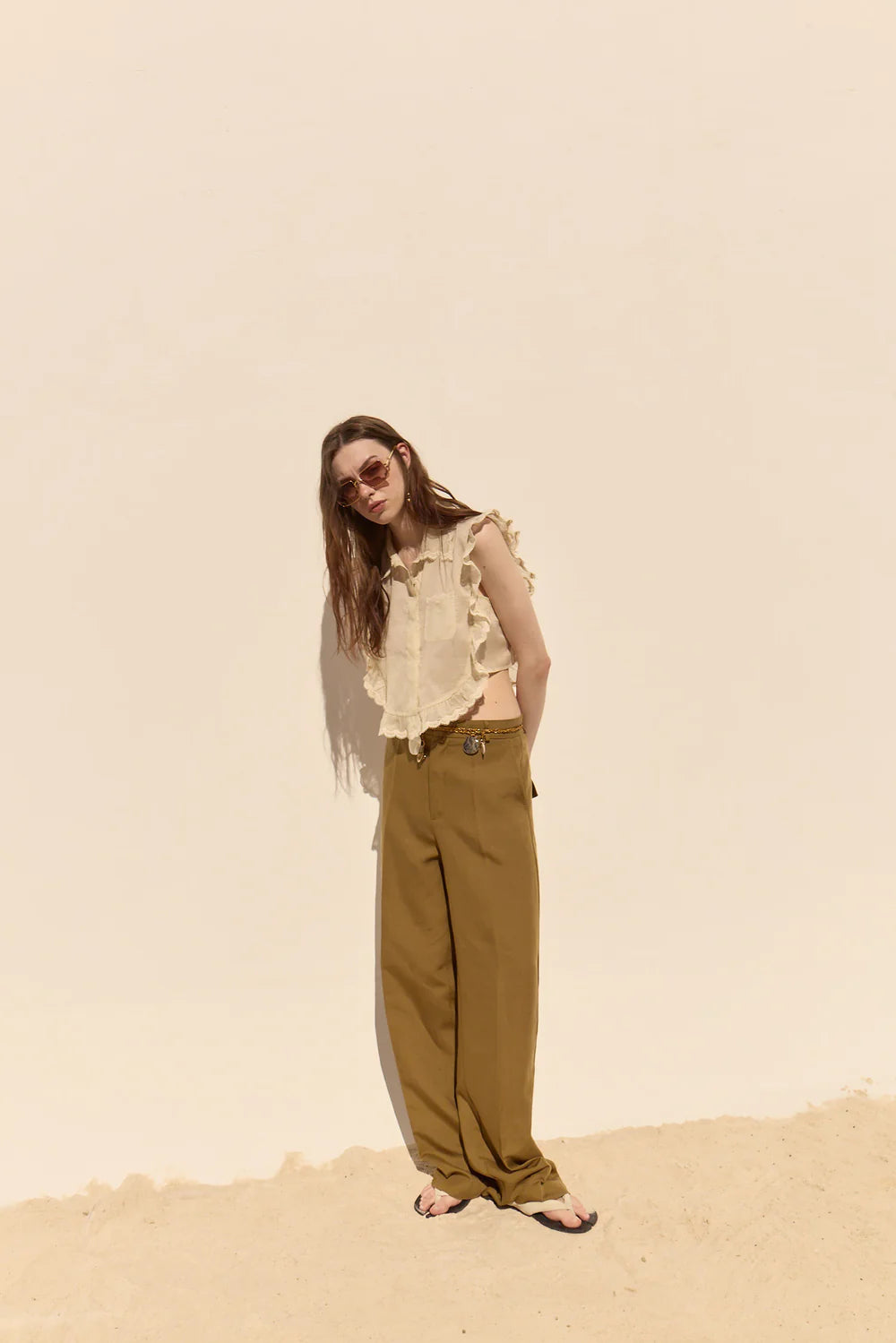 Woman in a beige top and green pants standing against a beige background