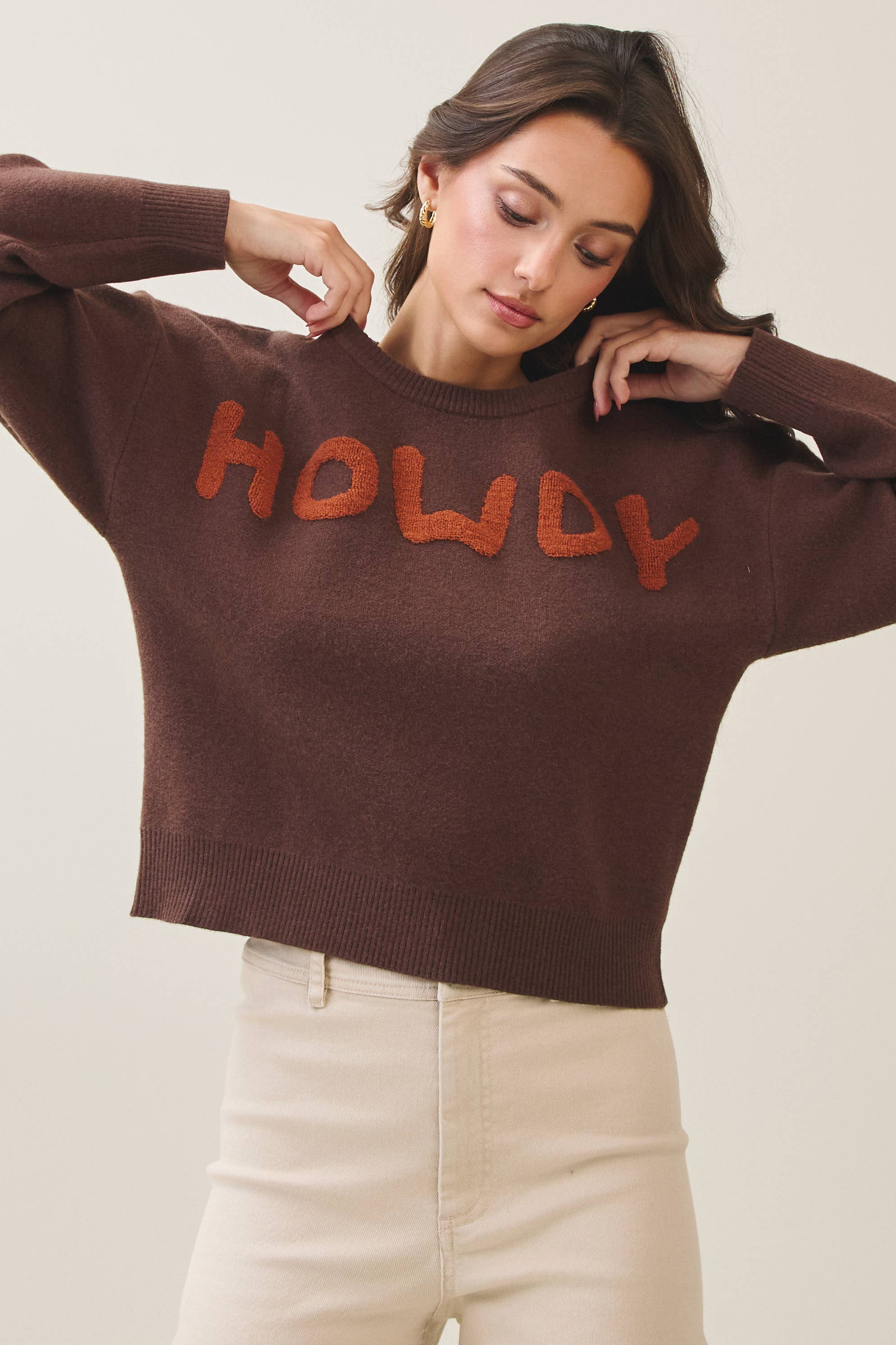 Woman wearing a brown sweater with 'HOWDY' text on a plain background