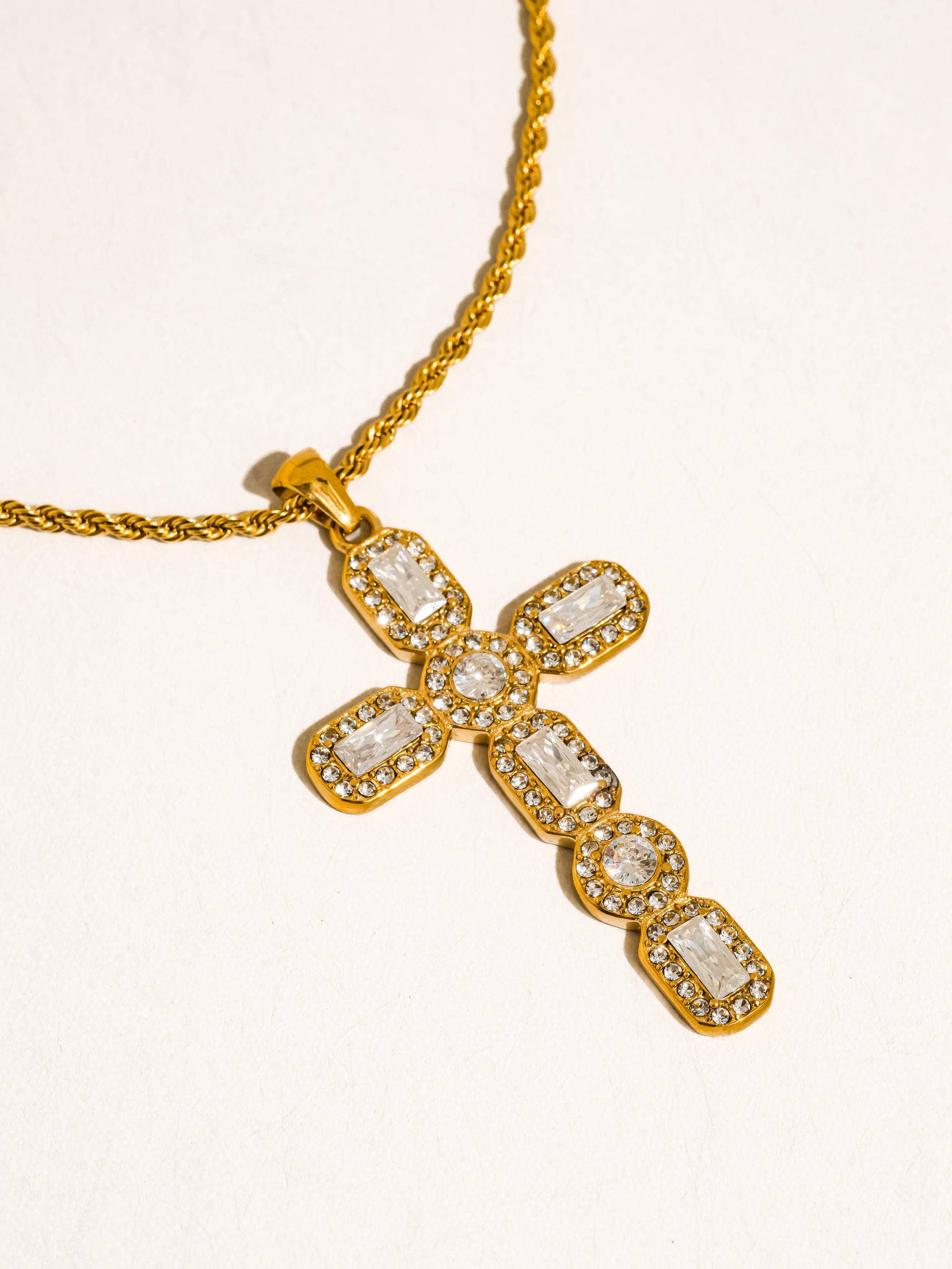 Gold cross necklace with clear gemstones on a white background