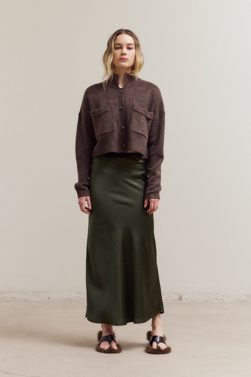 Woman wearing a brown cropped jacket and green skirt against a plain background