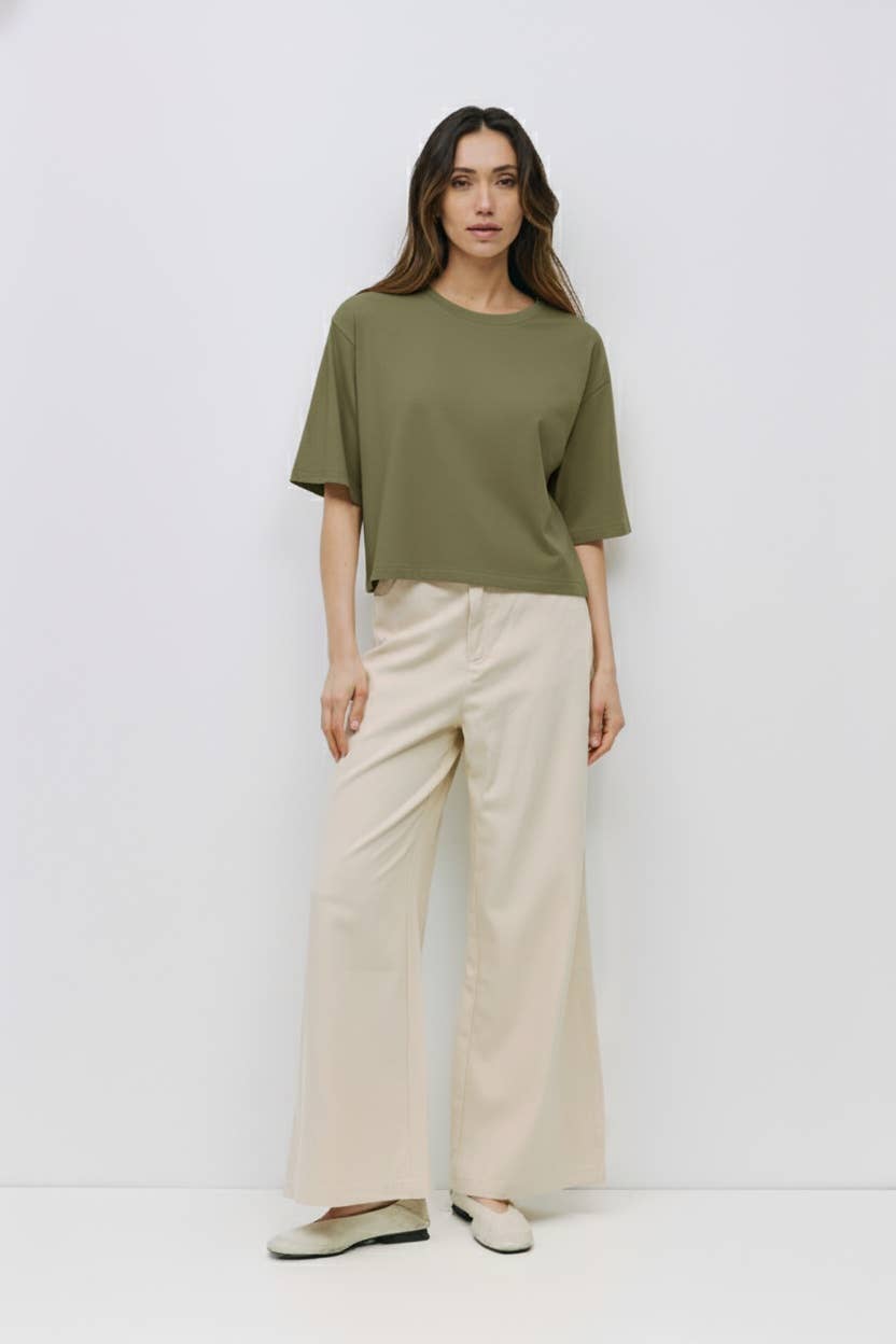 Woman wearing a green top and beige pants on a white background