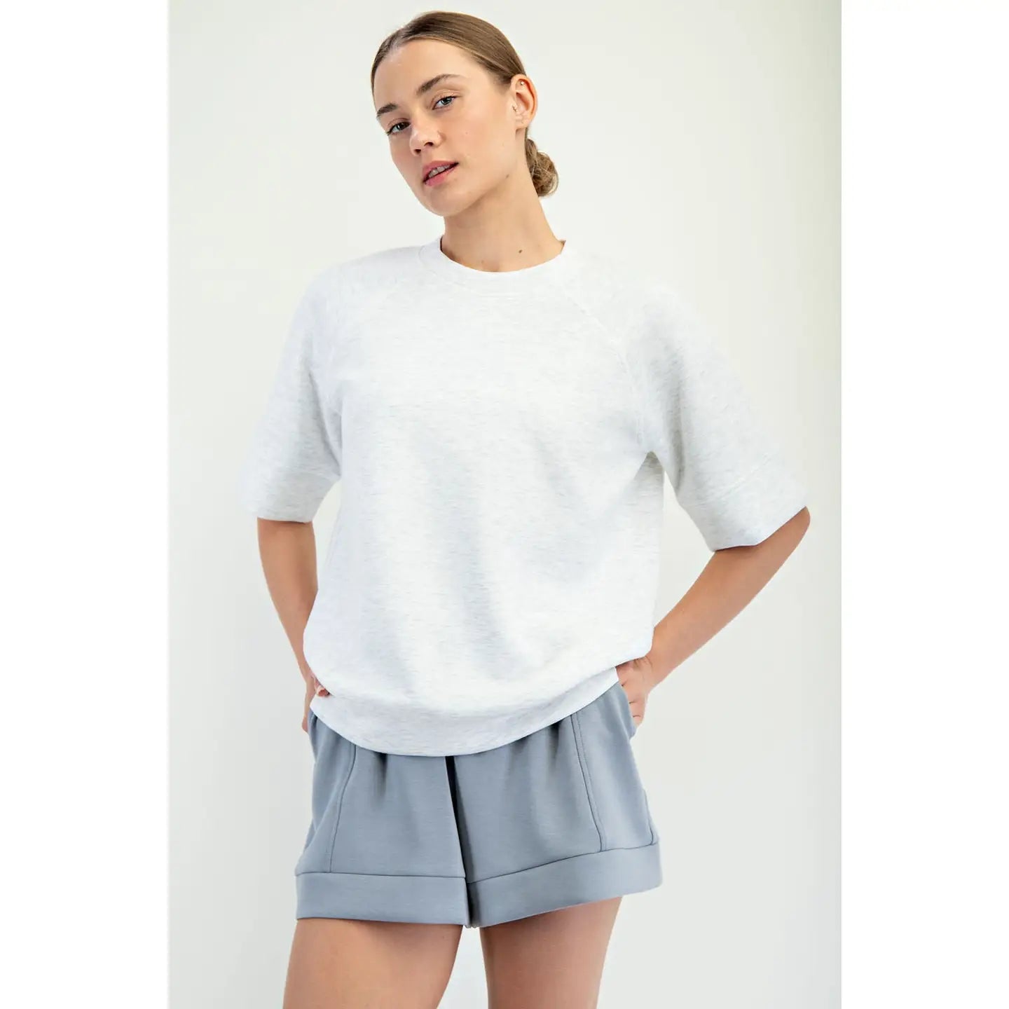 Woman wearing a light gray sweater and shorts on a white background