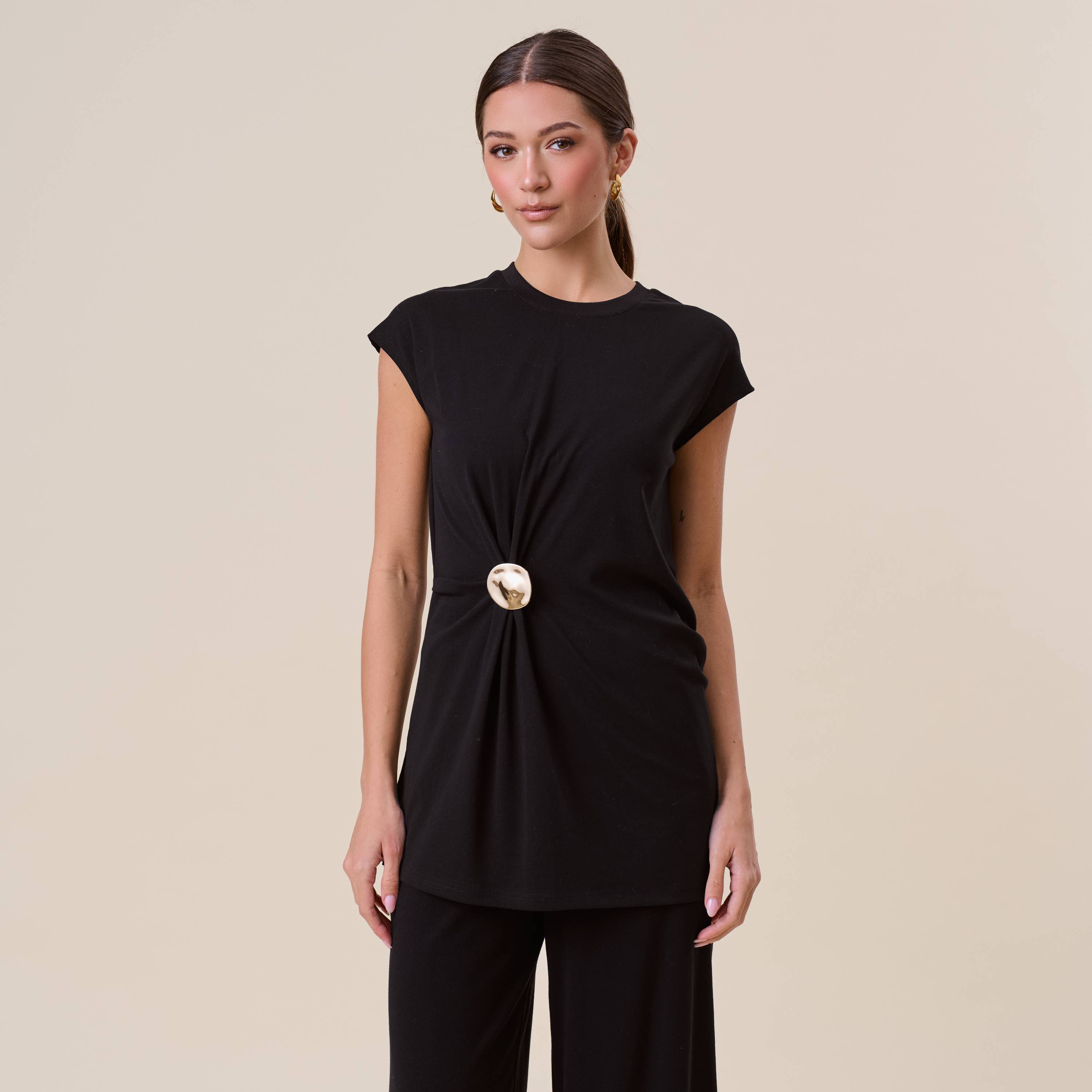 Woman wearing a black top with a gold button detail on a beige background