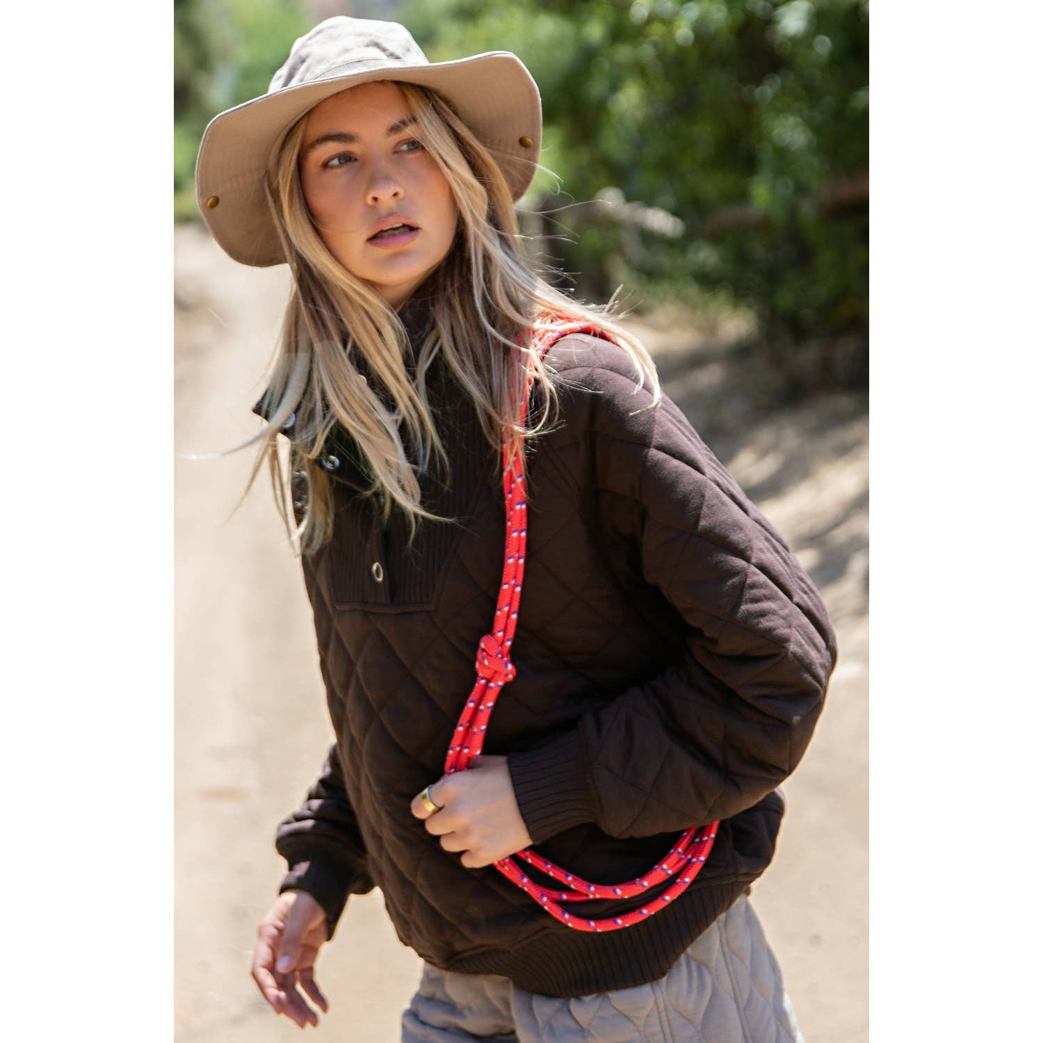 Person wearing a brown jacket and beige hat holding a red rope in a natural setting