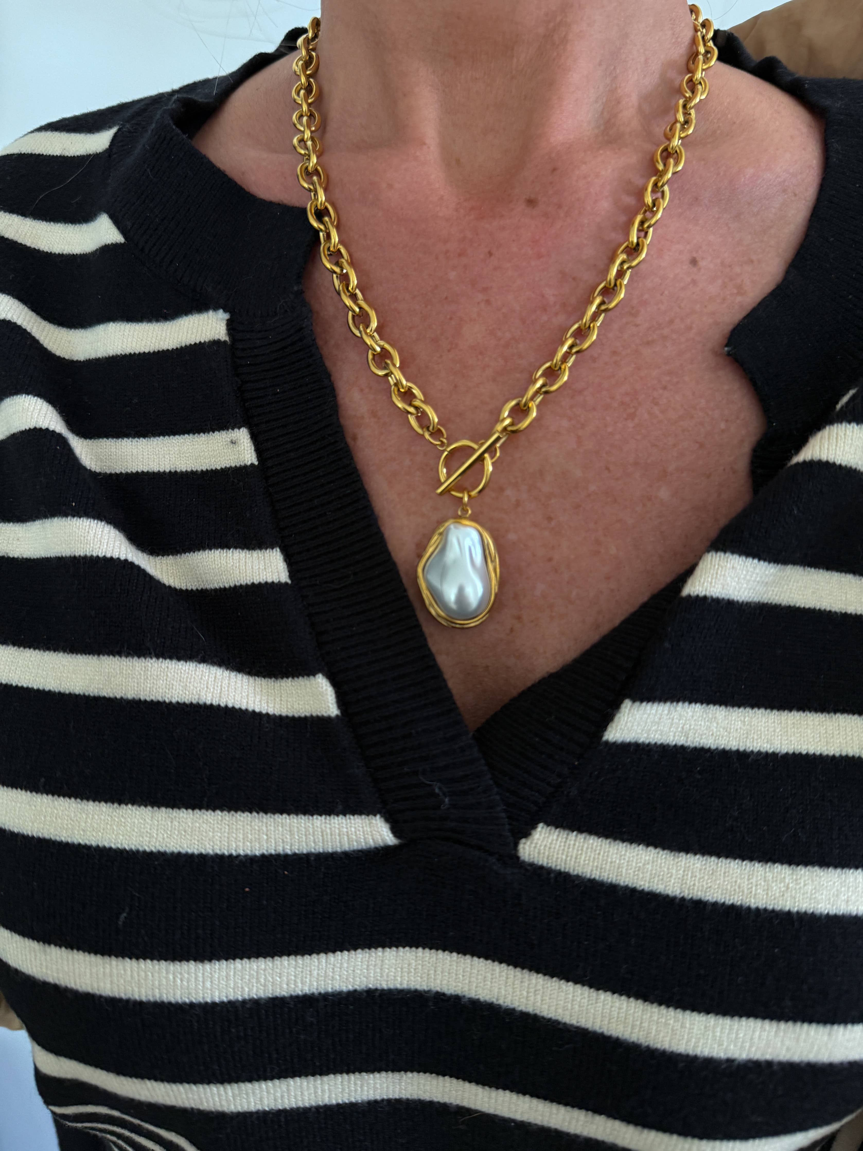 Gold chain necklace with a pendant worn by a person in a black and white striped shirt.