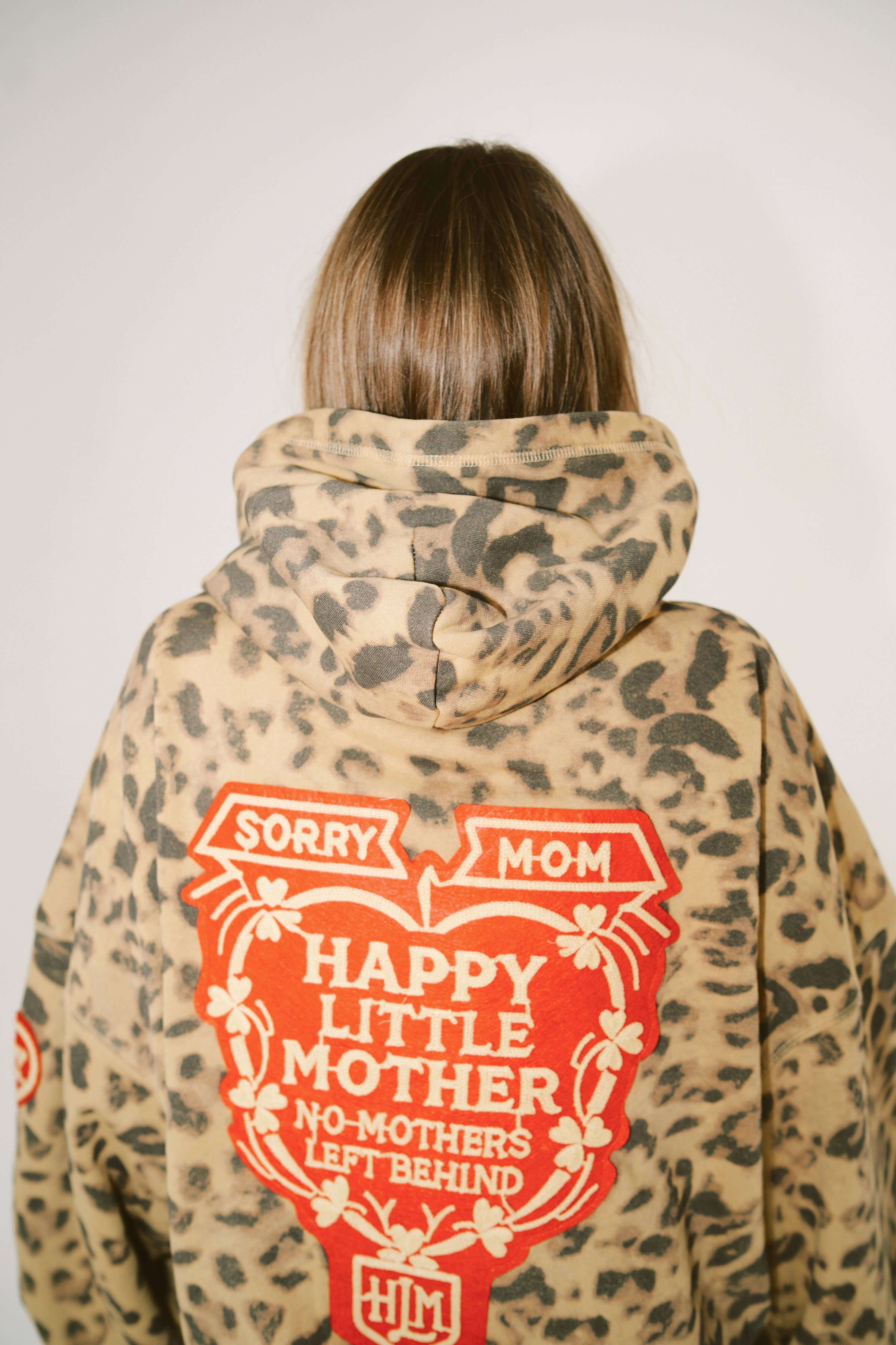 Person wearing a leopard print hoodie with red text on the back against a plain background