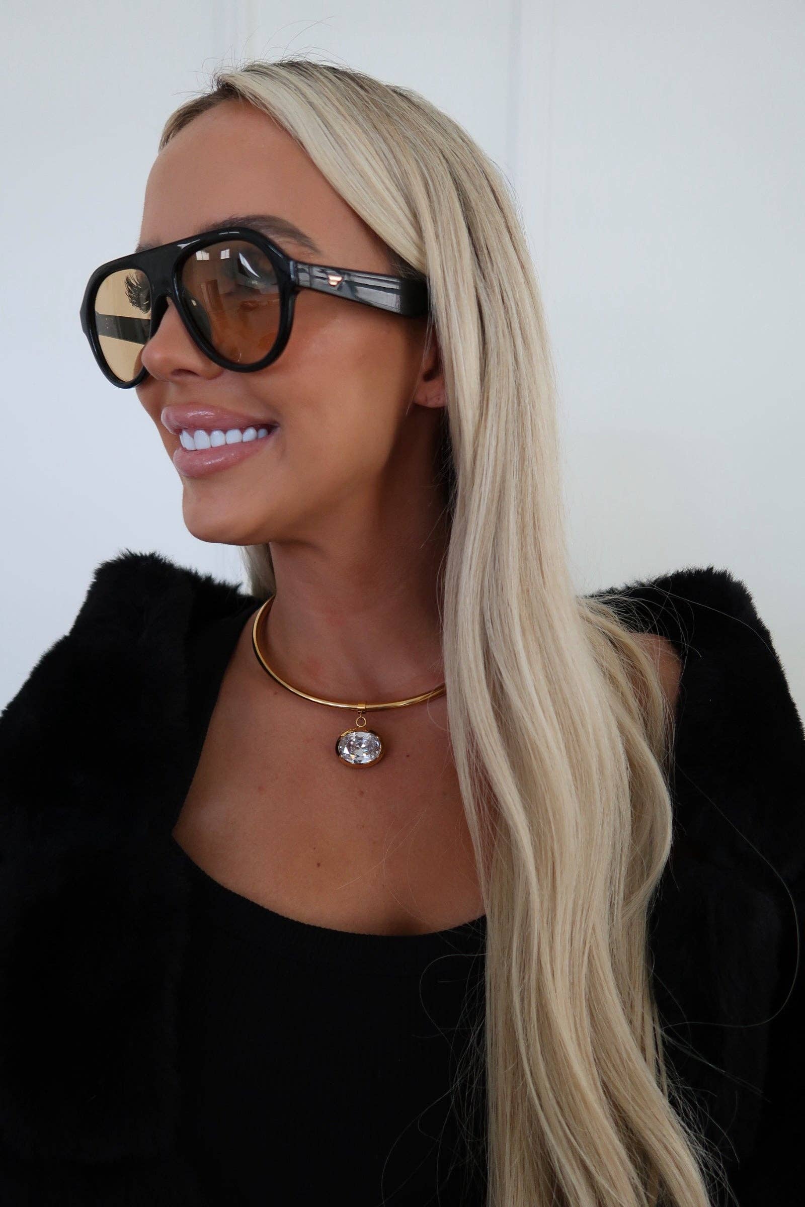Person with long blonde hair wearing sunglasses and a black outfit against a white background