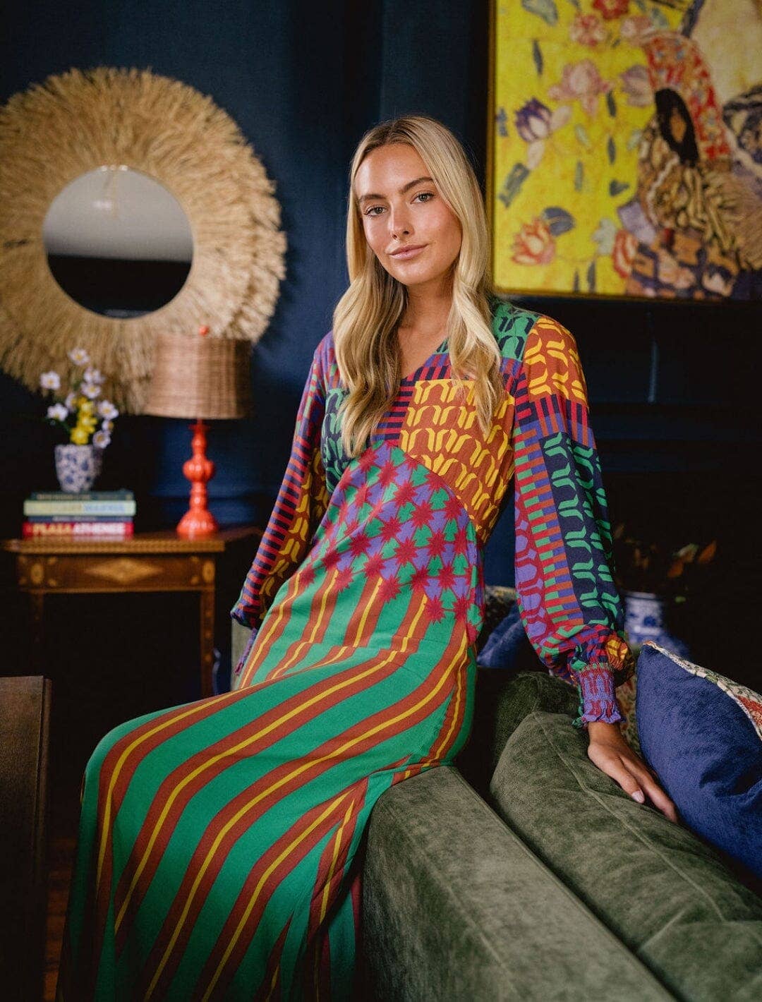 Woman in a colorful outfit sitting on a couch in a room with decorative elements.