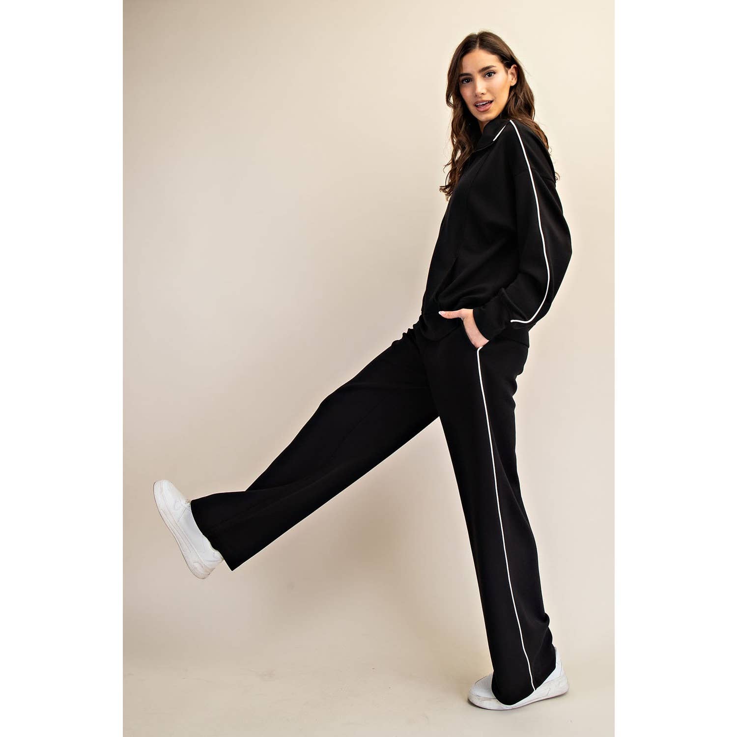 Woman wearing a black tracksuit with white piping on a beige background