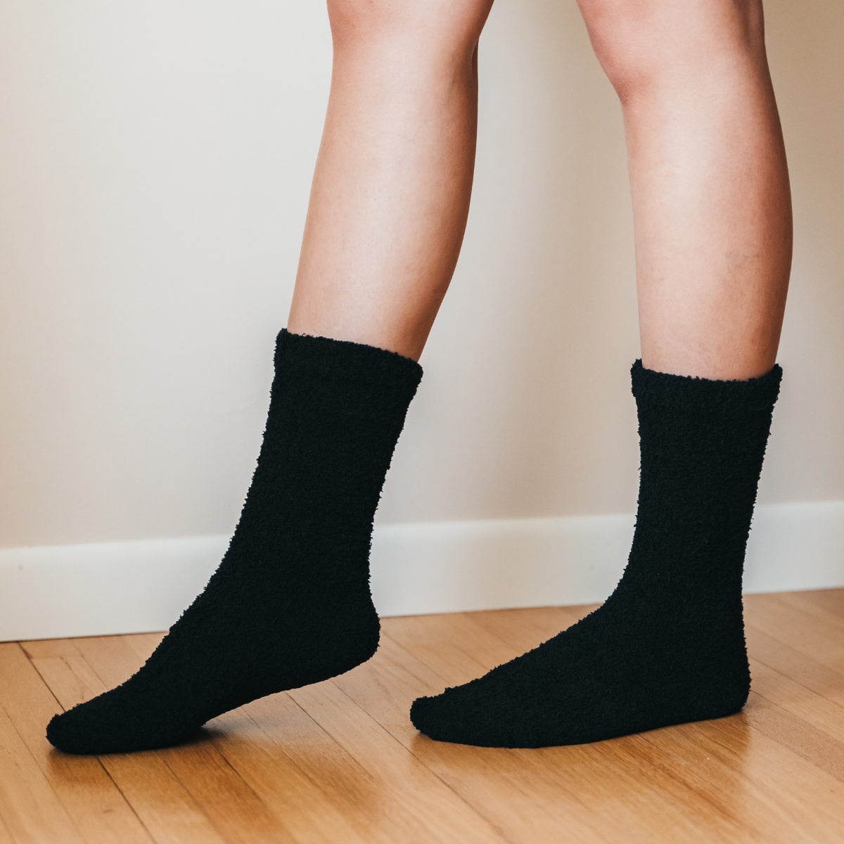 Person wearing black socks on a wooden floor with a neutral wall background