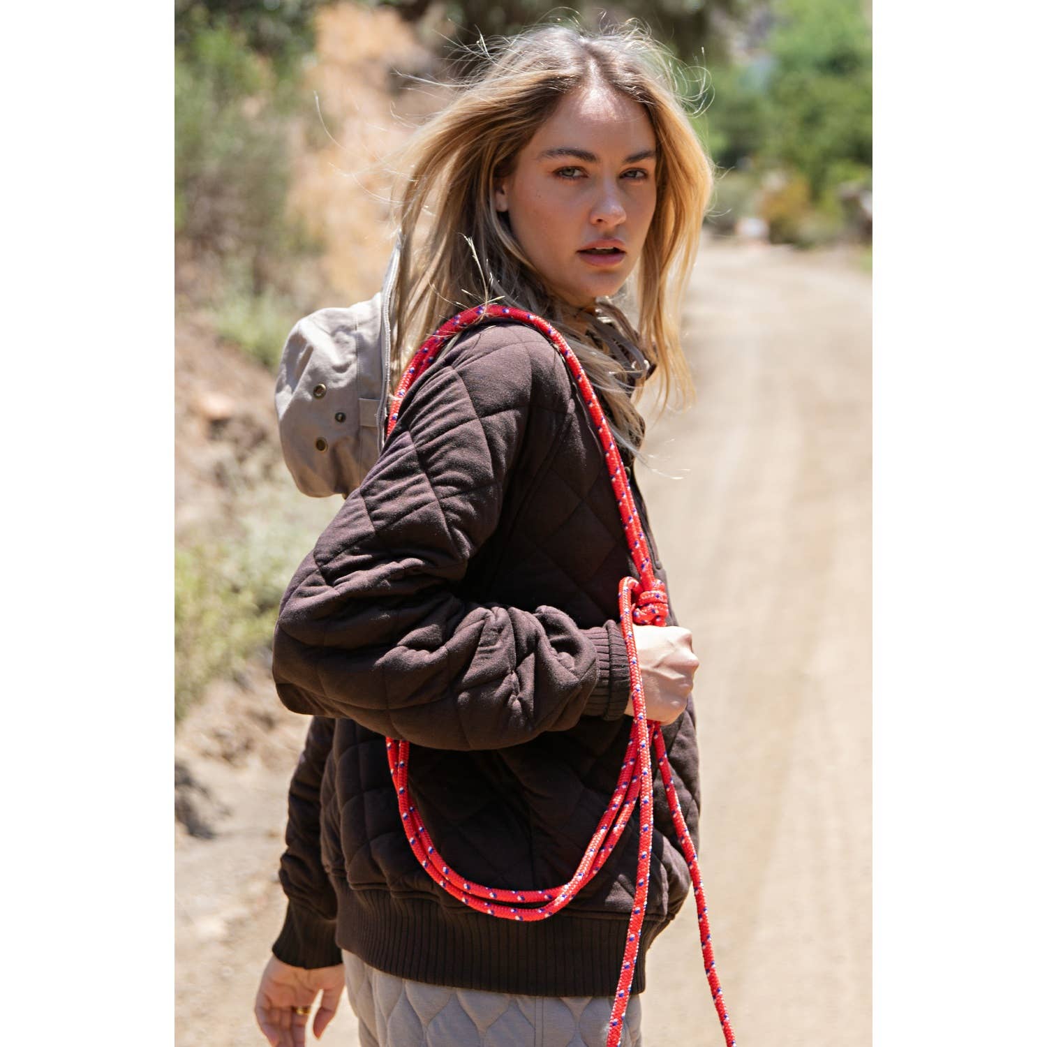 Woman holding a red lasso on a dirt road with greenery in the background
