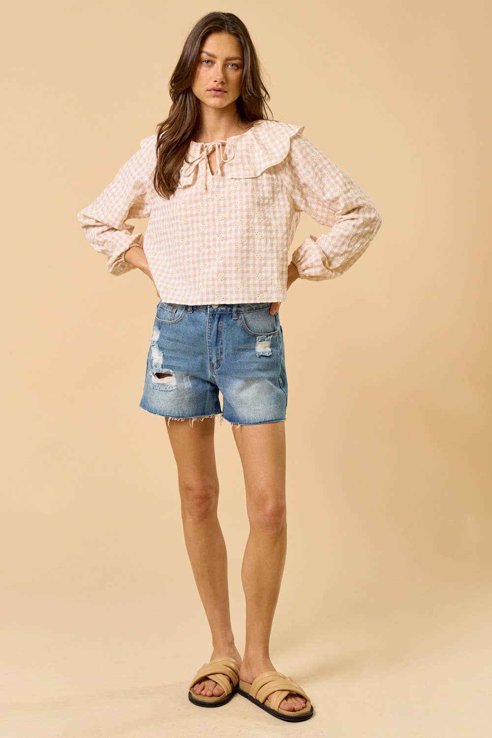 Woman wearing a checkered blouse and denim shorts on a beige background