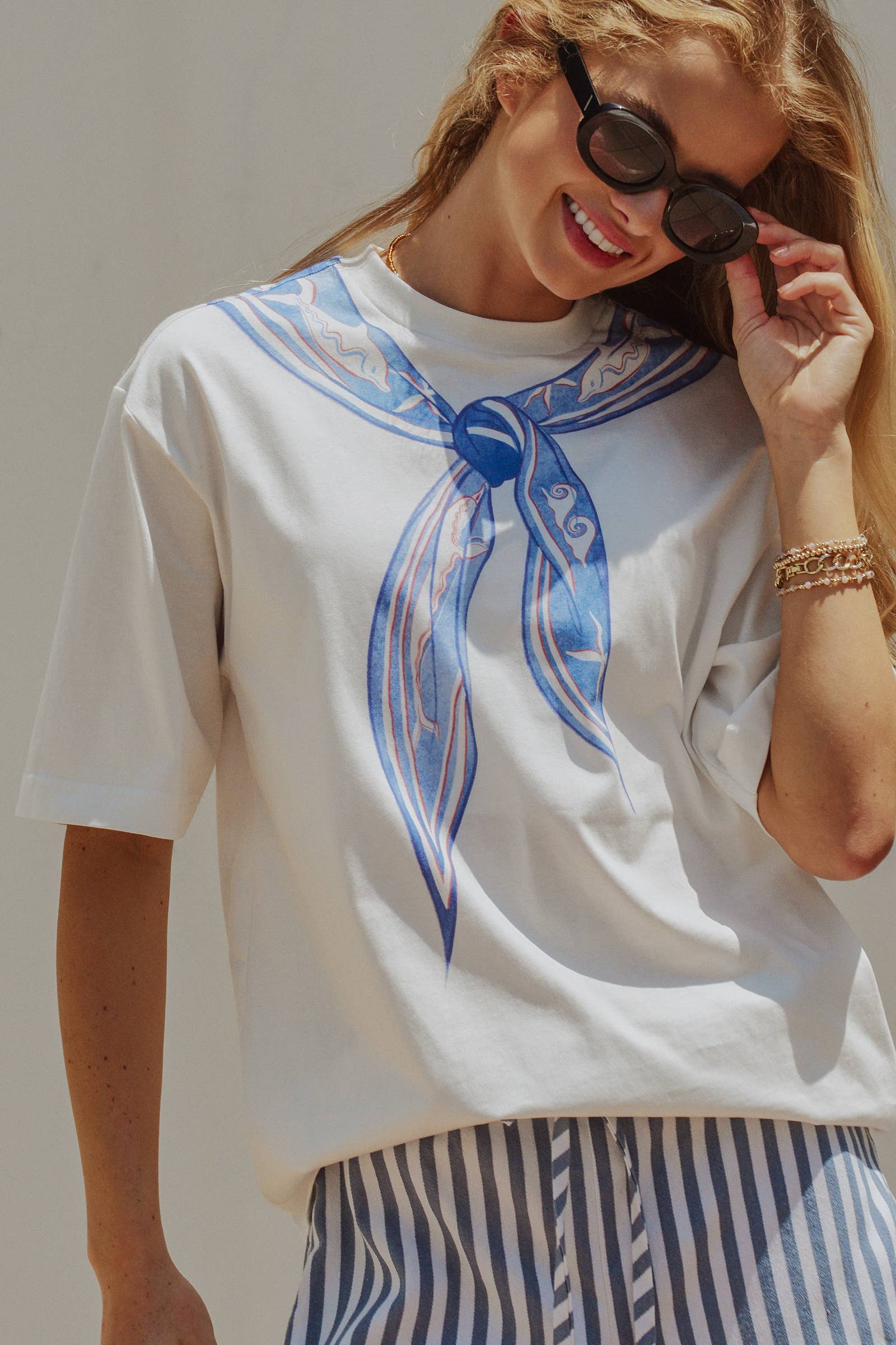 Woman wearing a white t-shirt with a blue graphic design, striped pants, and sunglasses.