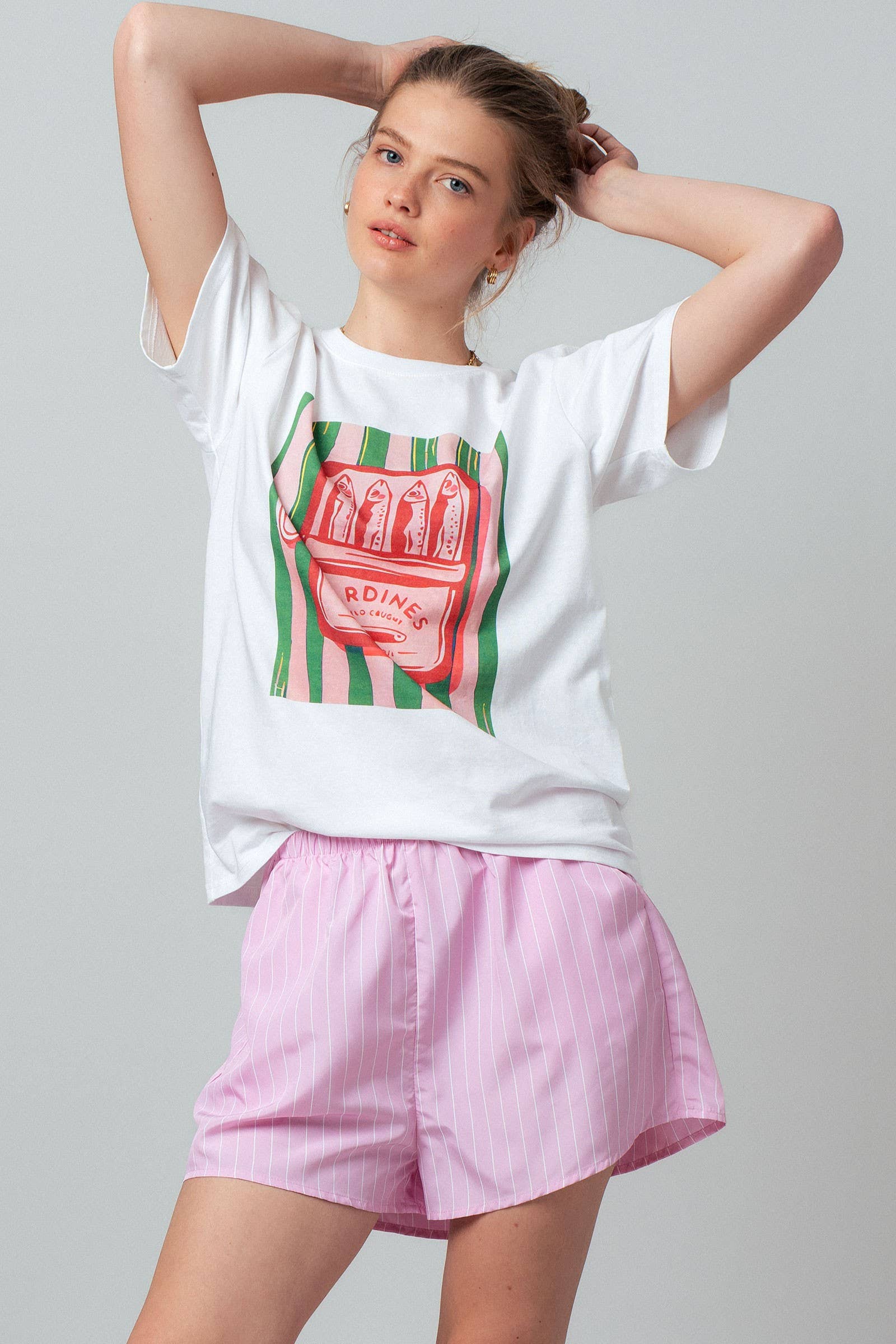 Person wearing a white t-shirt with a graphic design and pink shorts on a gray background
