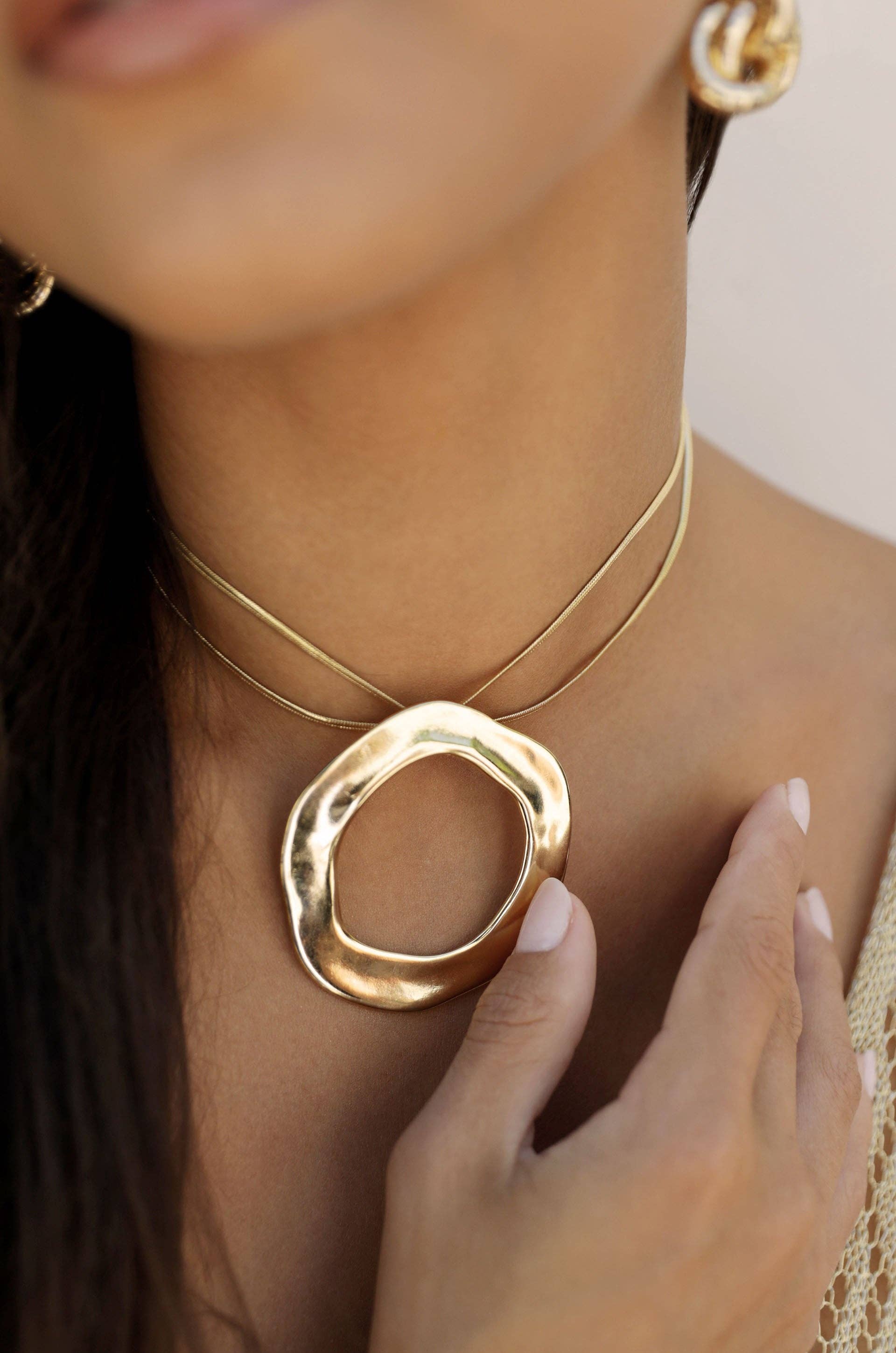 Gold necklace with a large circular pendant worn by a person.