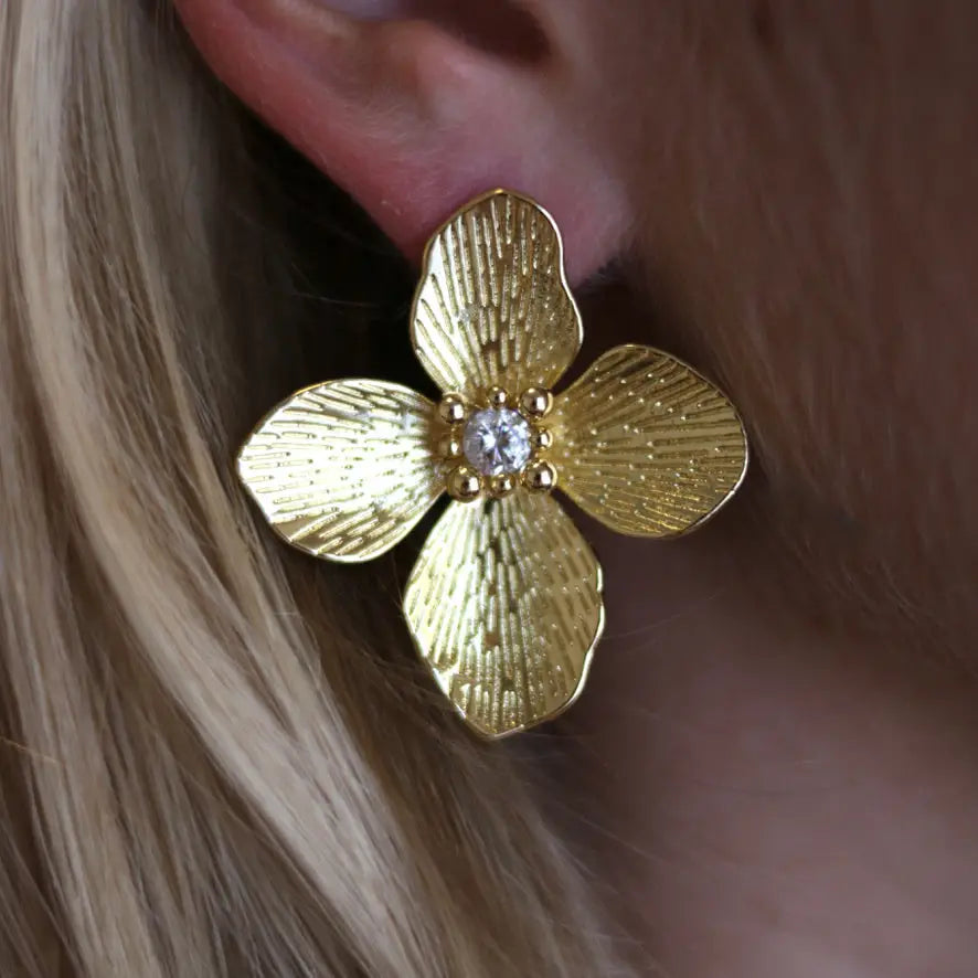 Gold flower-shaped earring with a diamond on an ear