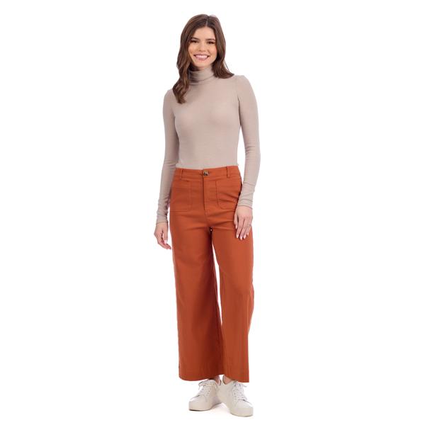 Woman wearing a beige turtleneck and rust-colored pants on a white background