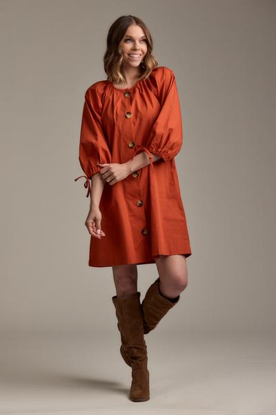 Woman wearing an orange dress with puff sleeves and brown boots on a plain background