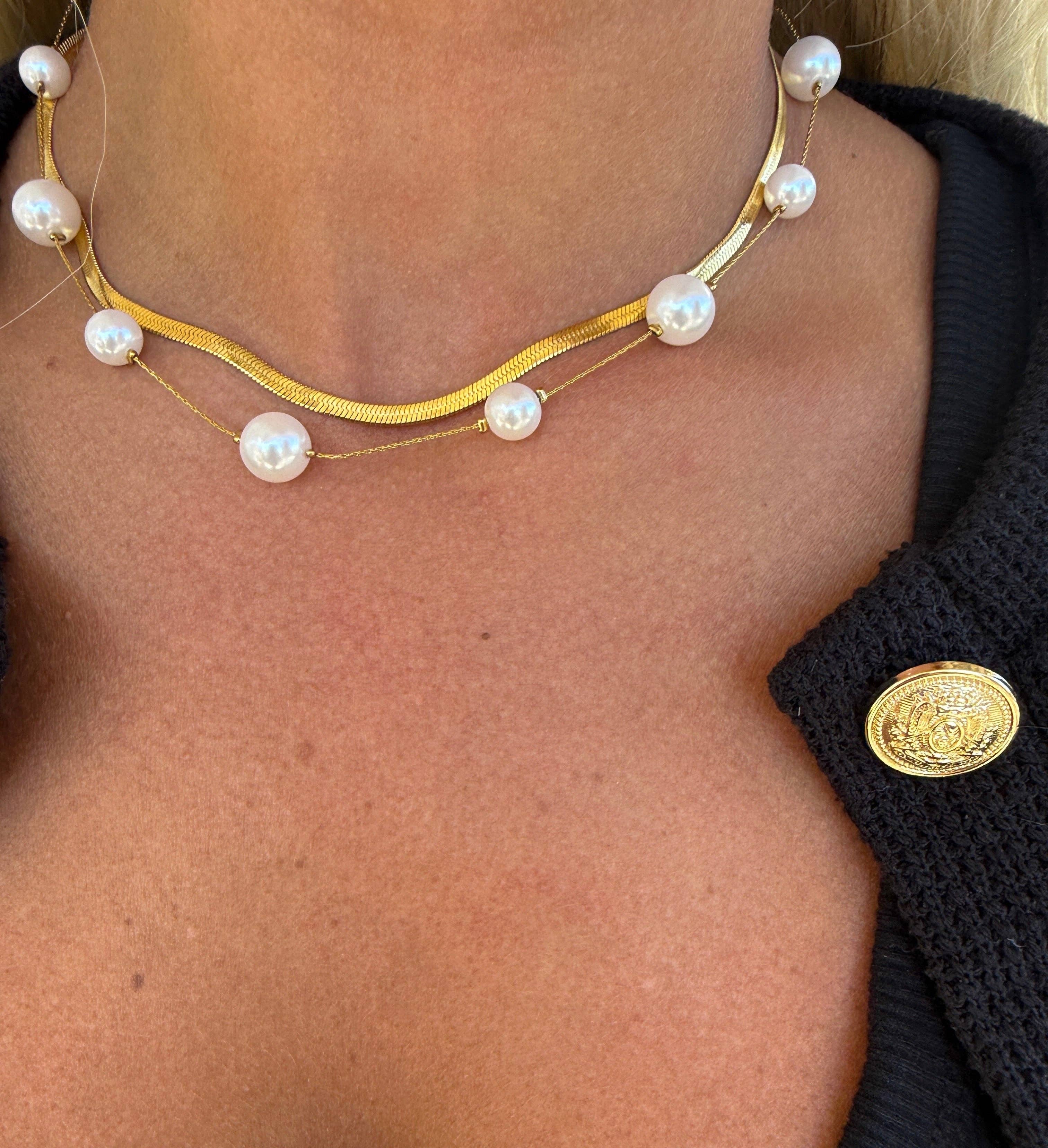 Gold necklace with pearls worn by a person, close-up view.