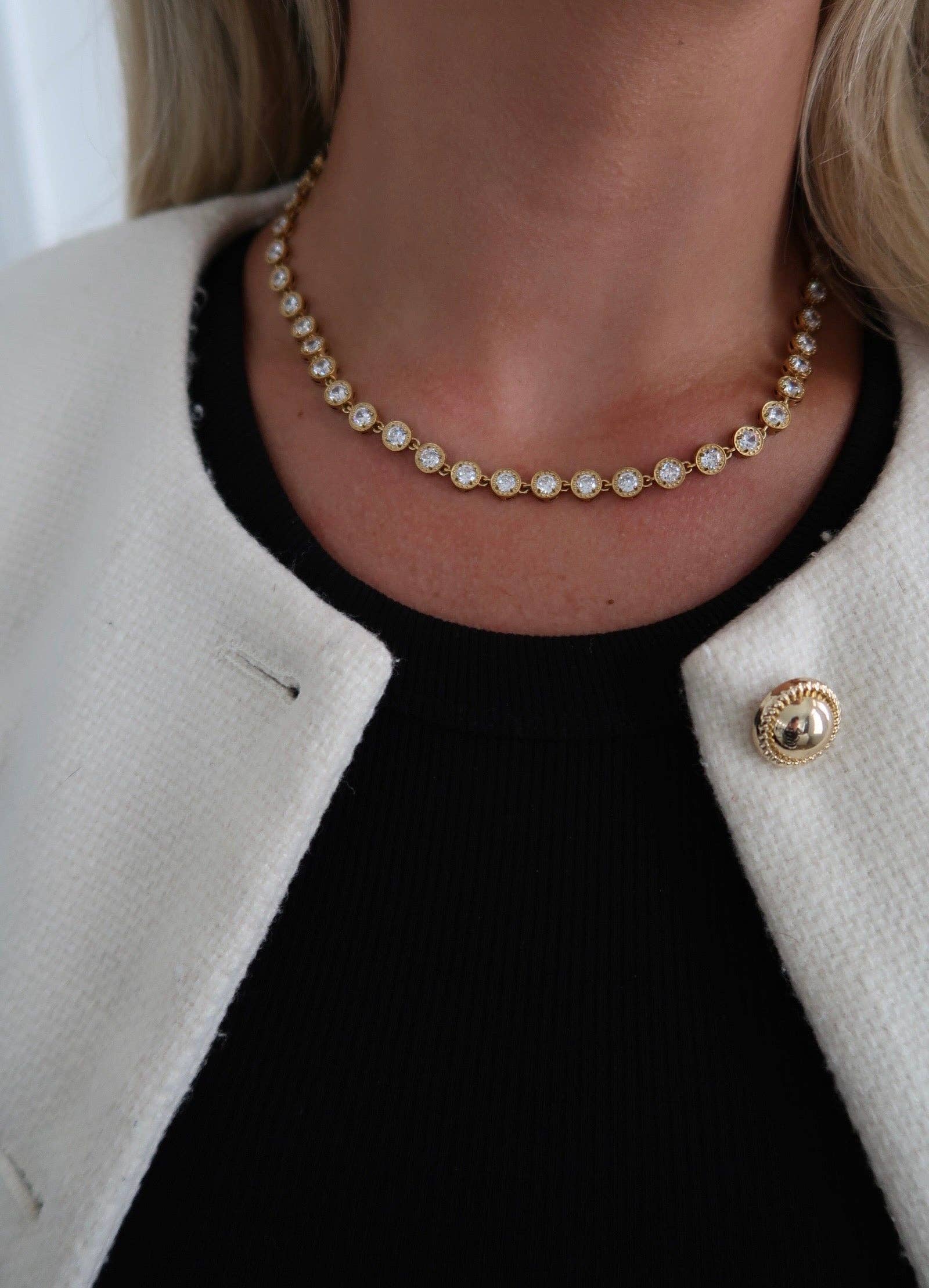 Close-up of a person wearing a pearl necklace with a black top and beige jacket.