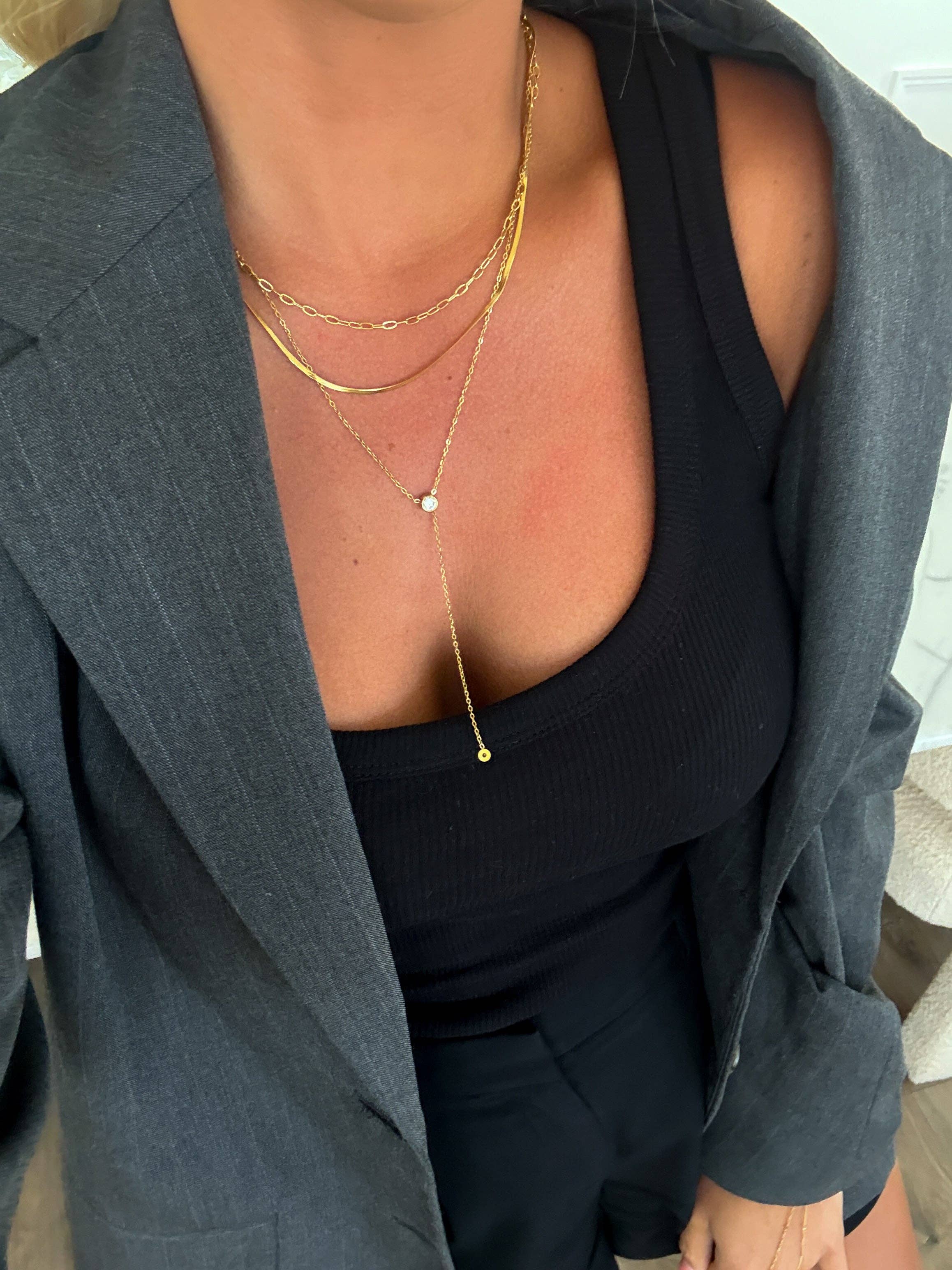 Person wearing a gray blazer over a black top with layered gold necklaces.