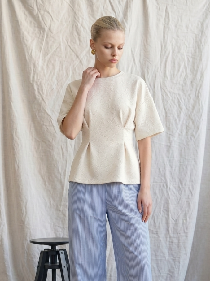 Woman wearing a beige top and light blue striped pants against a white background