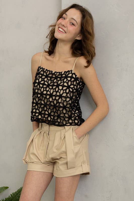 Woman wearing a black patterned top and beige shorts against a plain background