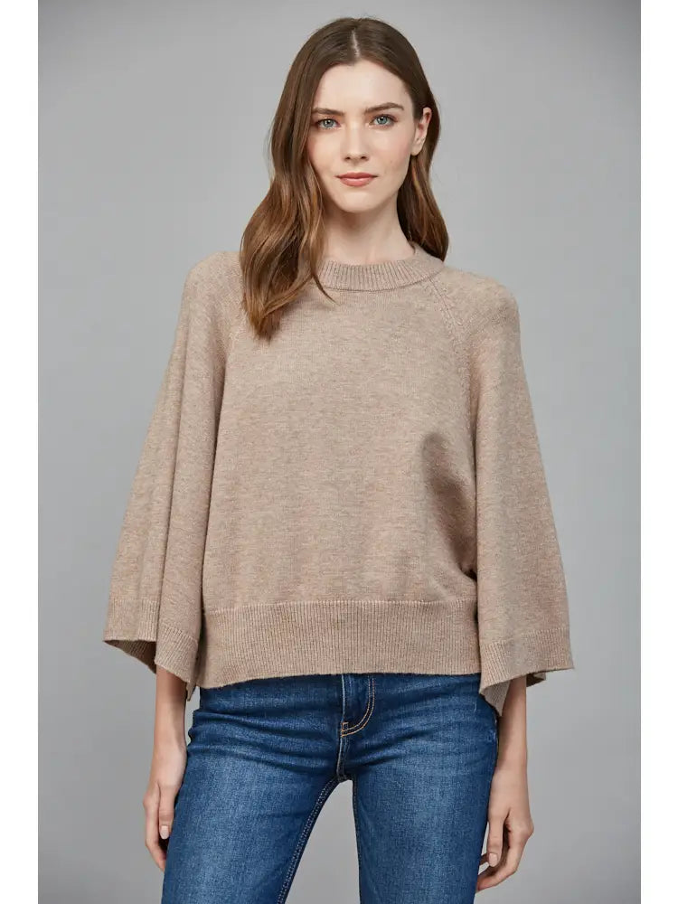 Woman wearing a beige sweater and blue jeans against a gray background