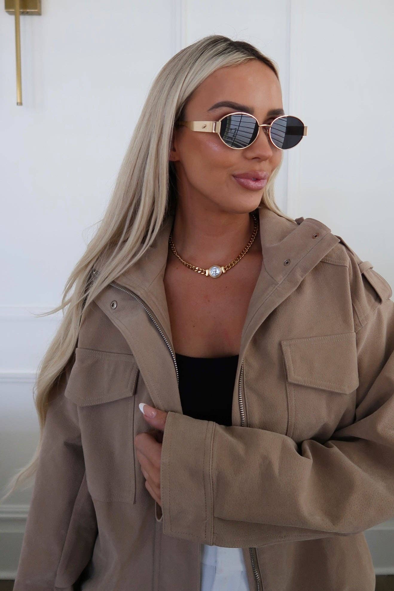Woman wearing a beige jacket and sunglasses with a neutral background