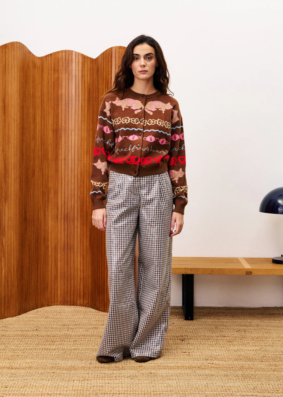 Woman wearing a patterned sweater and checkered pants in a room with wooden paneling.