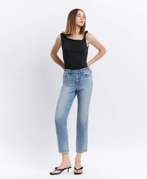 Woman wearing a black sleeveless top and light blue jeans on a white background
