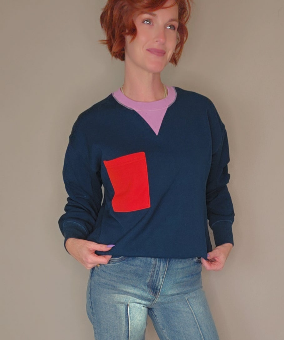 Person wearing a navy sweater with a red pocket and light blue jeans against a beige background