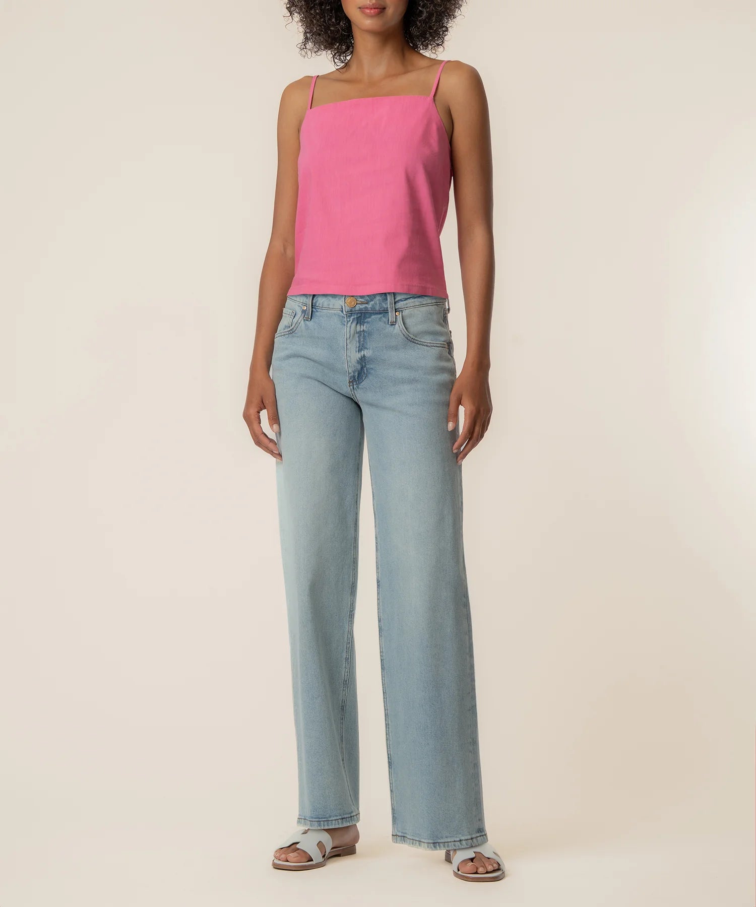 Woman wearing a pink top and light blue jeans on a beige background