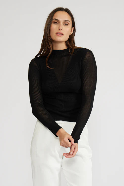 Woman wearing a black long-sleeve top and white pants on a white background