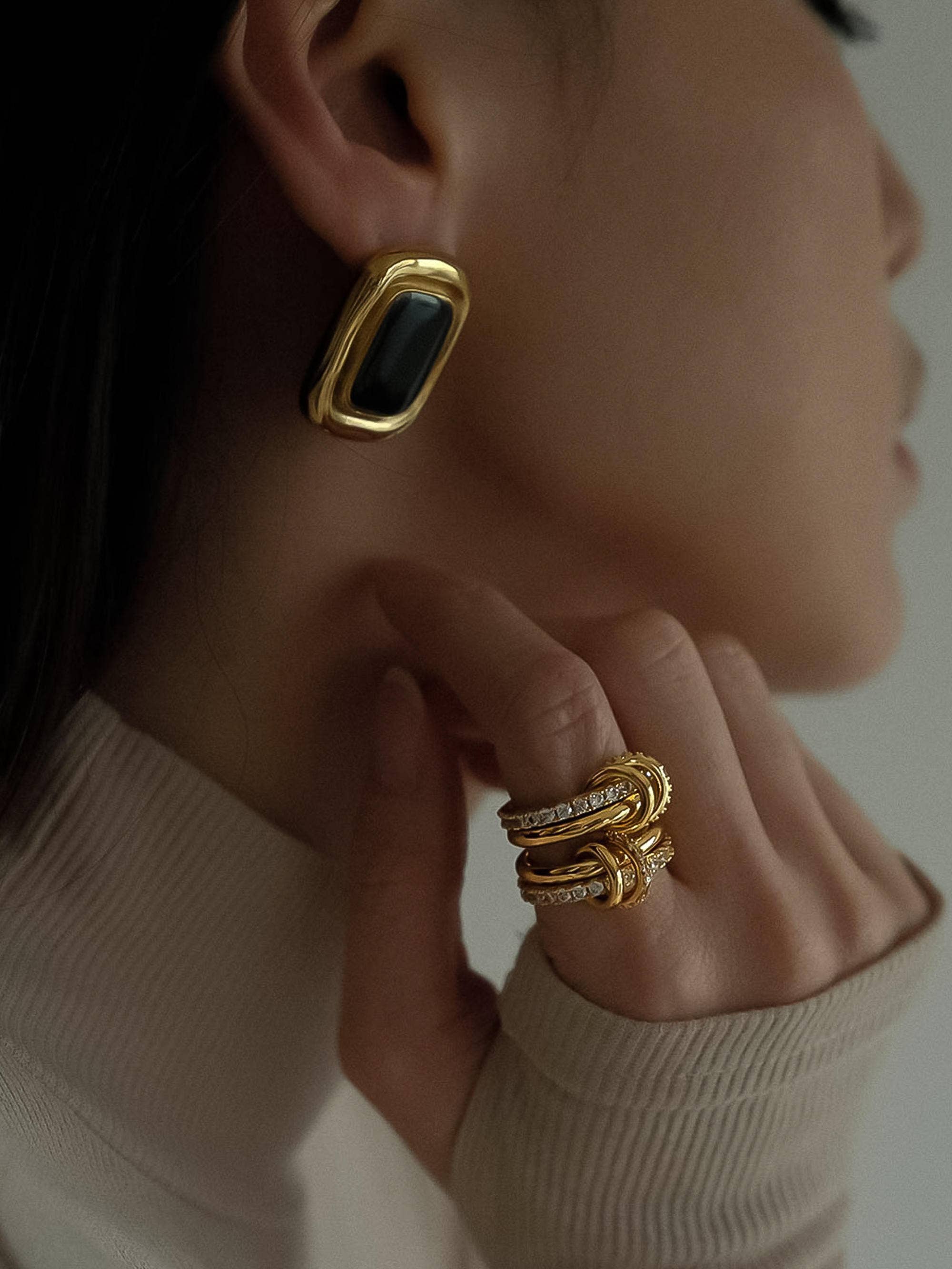 Close-up of a person wearing gold earrings and rings with a neutral background