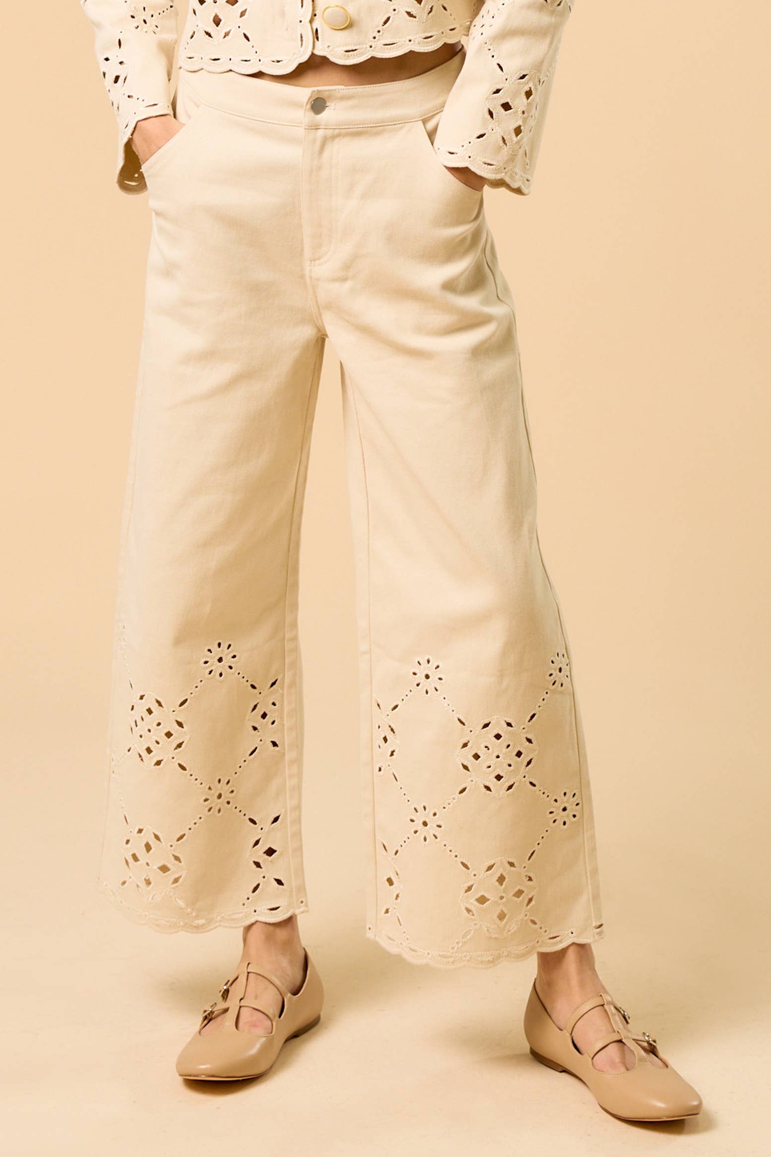 Person wearing cream-colored pants with eyelet details on a beige background