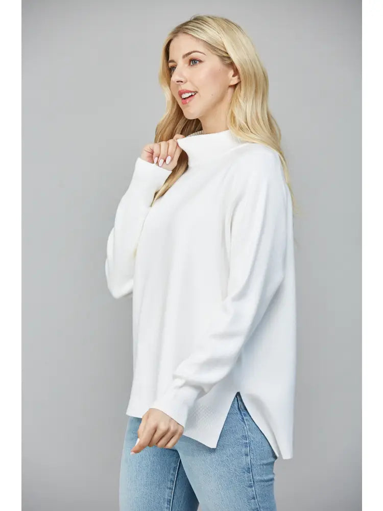 Woman wearing a white sweater and blue jeans against a gray background