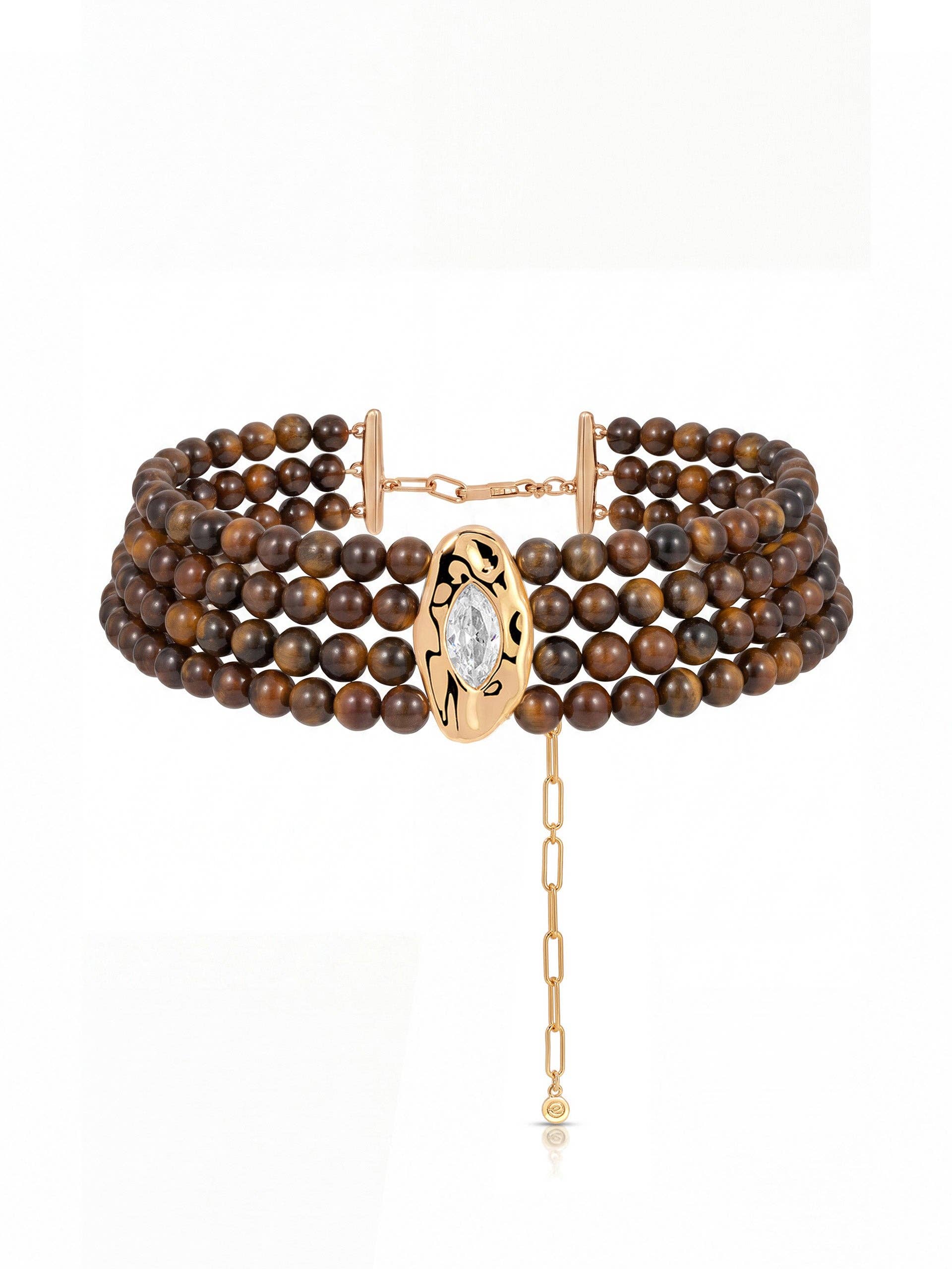 A multi-strand beaded choker necklace featuring brown tiger's eye beads and a gold-tone central oval charm with a clear marquise-cut gemstone and an extender chain.