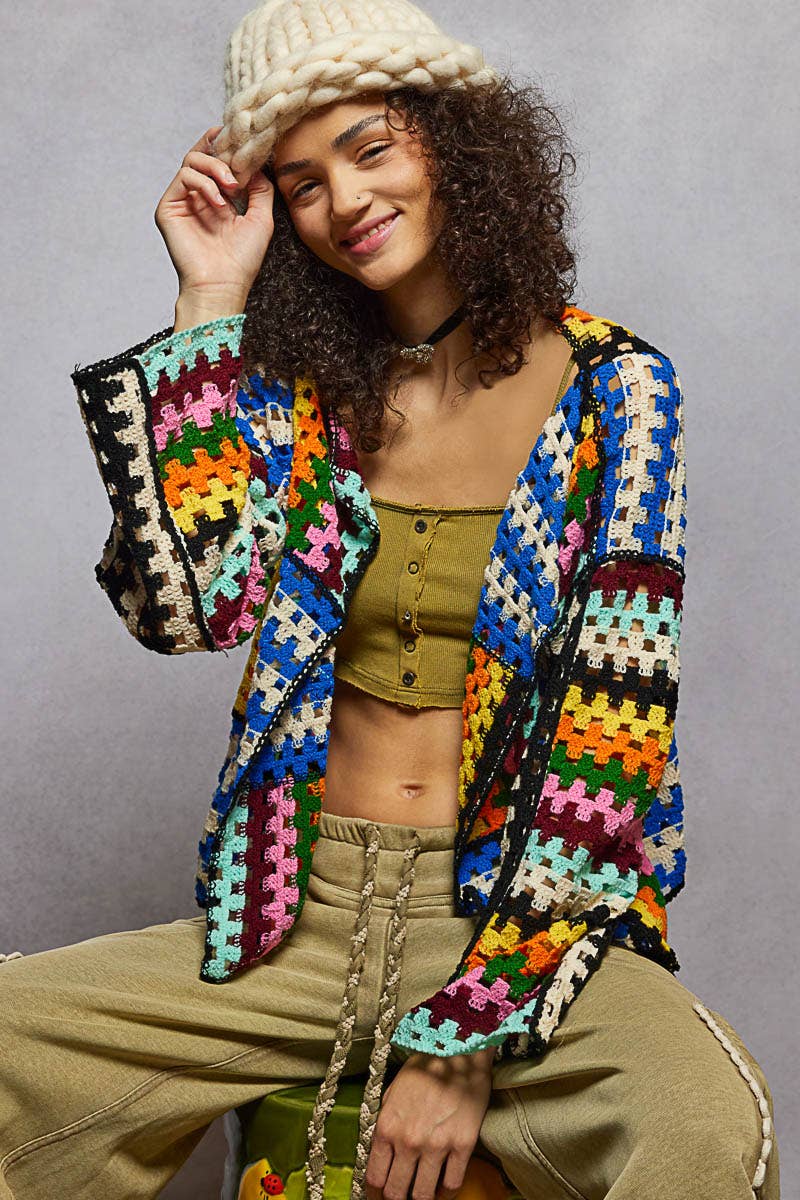 Person wearing a colorful crochet cardigan against a gray background
