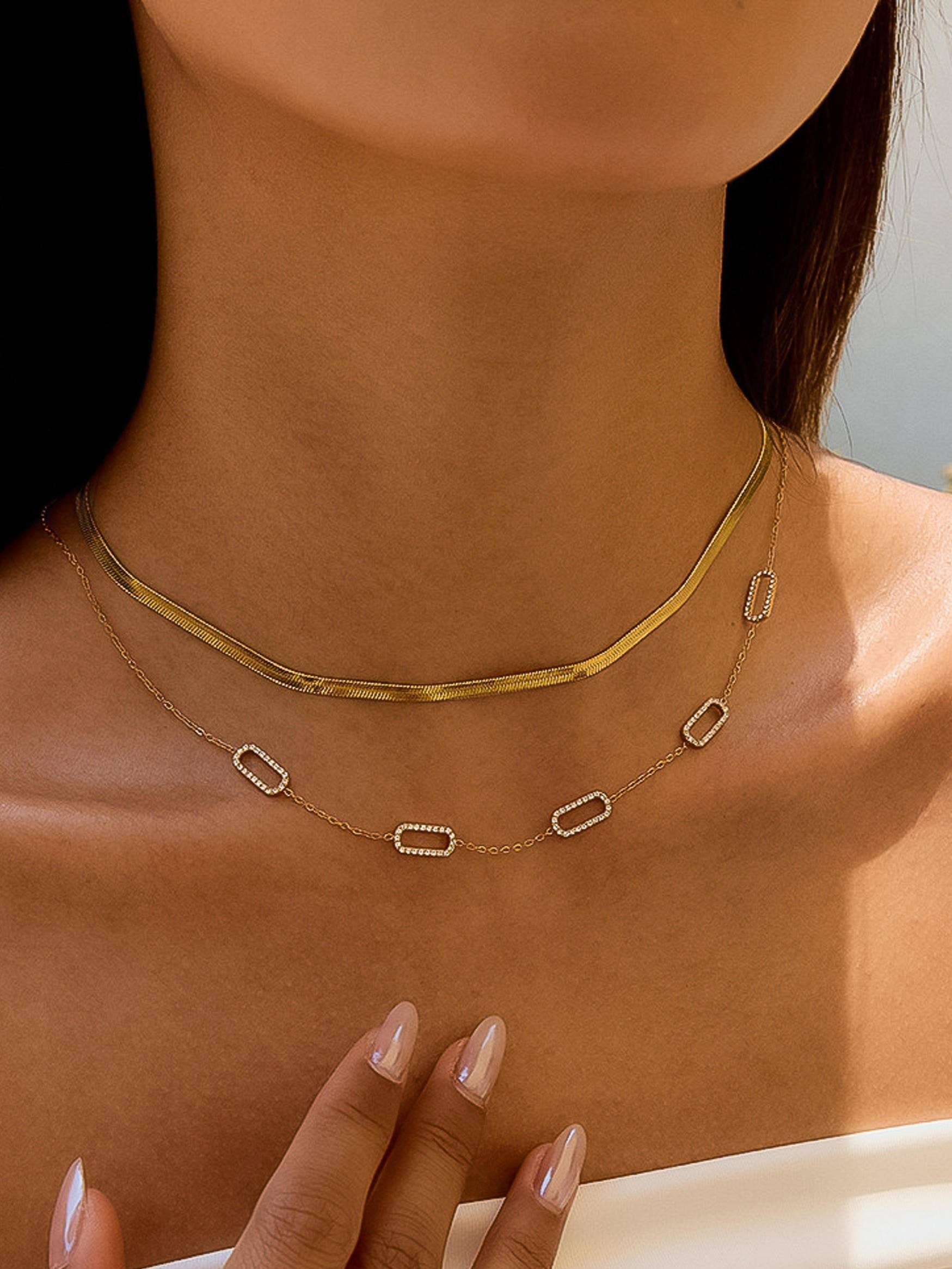 Gold necklace with geometric pendants on a person's neck