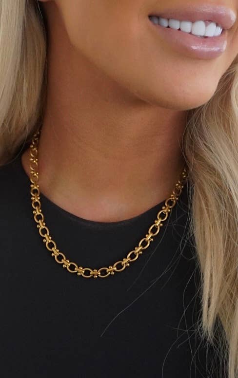 Gold chain necklace worn by a person with a blurred background