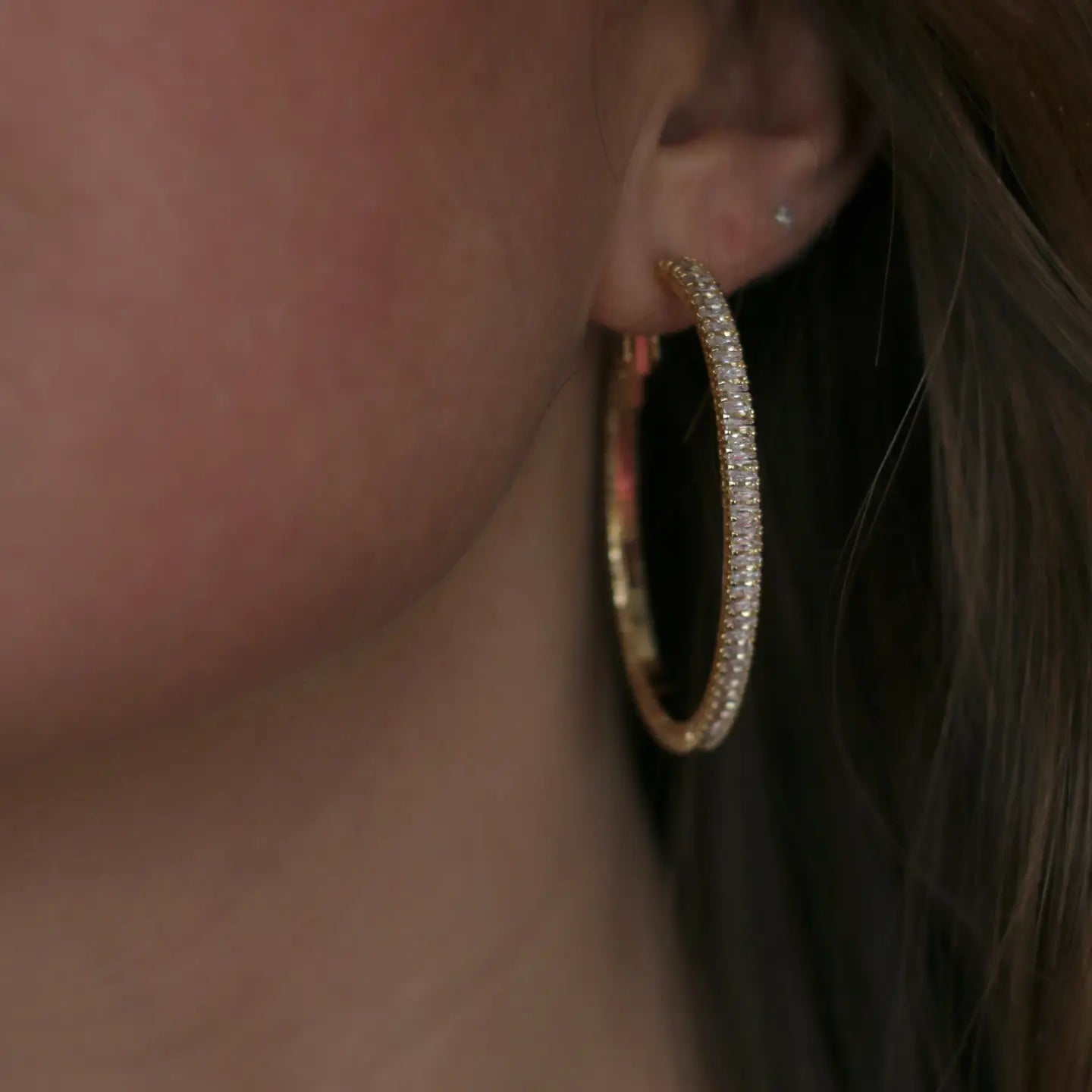 Close-up of a person wearing gold hoop earrings with a blurred background