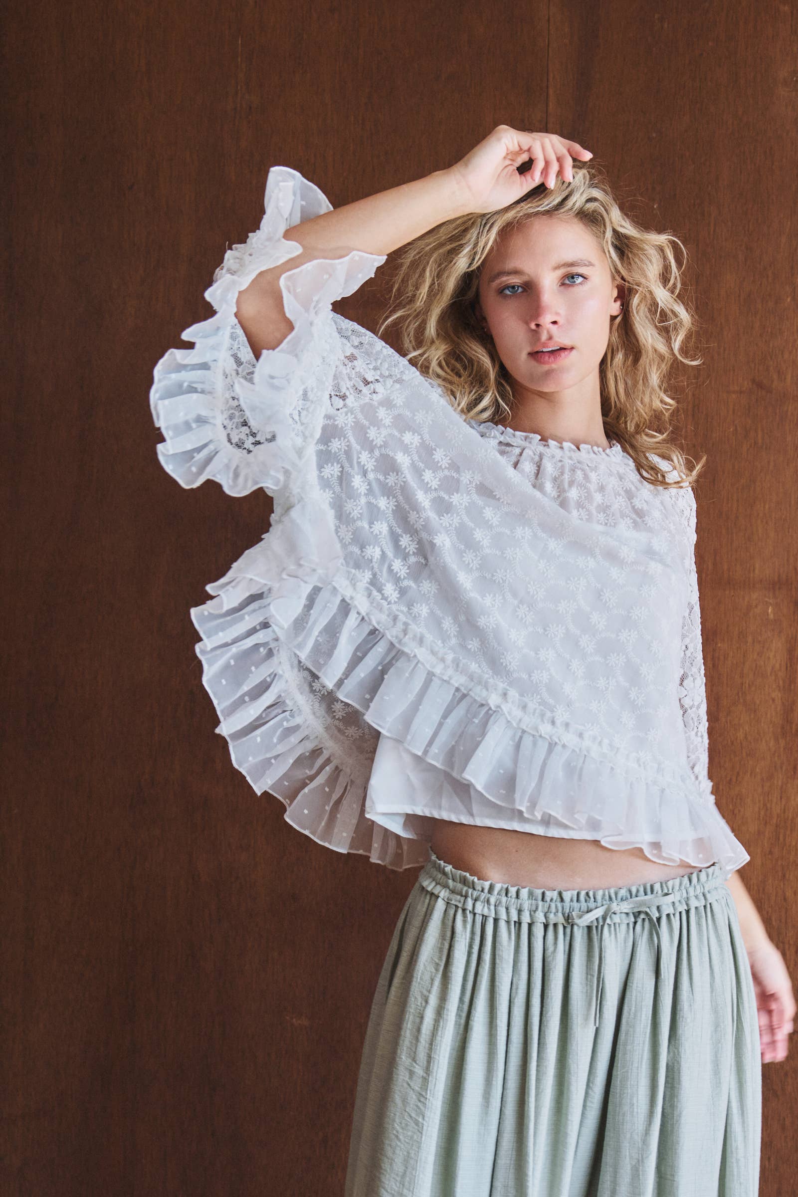 Woman wearing a white lace top and light green skirt against a brown background