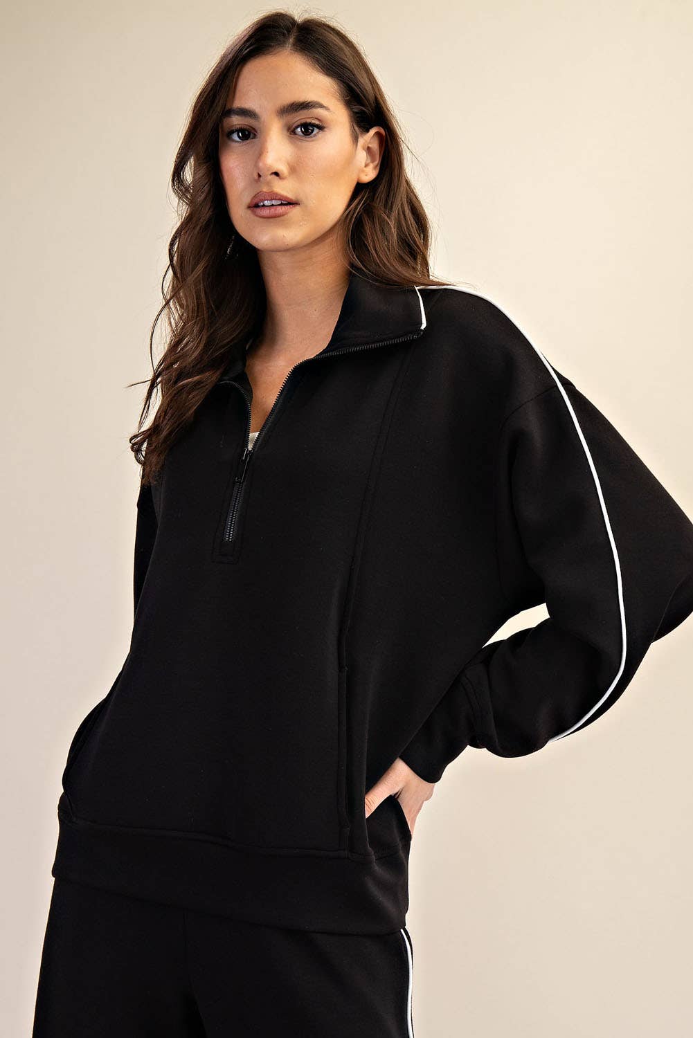 Woman wearing a black tracksuit with white piping on a beige background