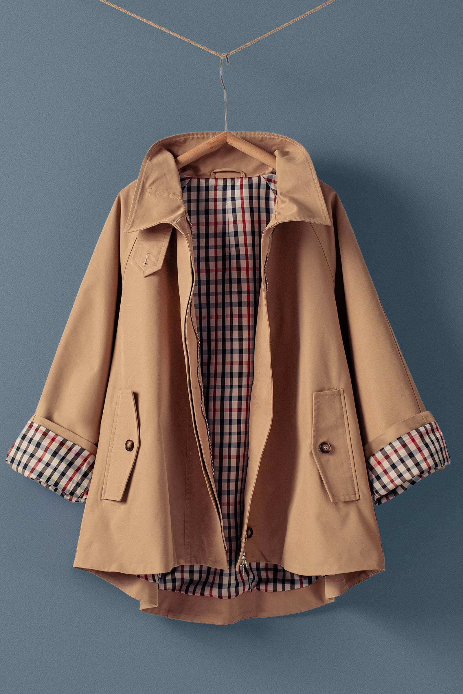 Tan coat with plaid lining and cuffs on a hanger against a blue background